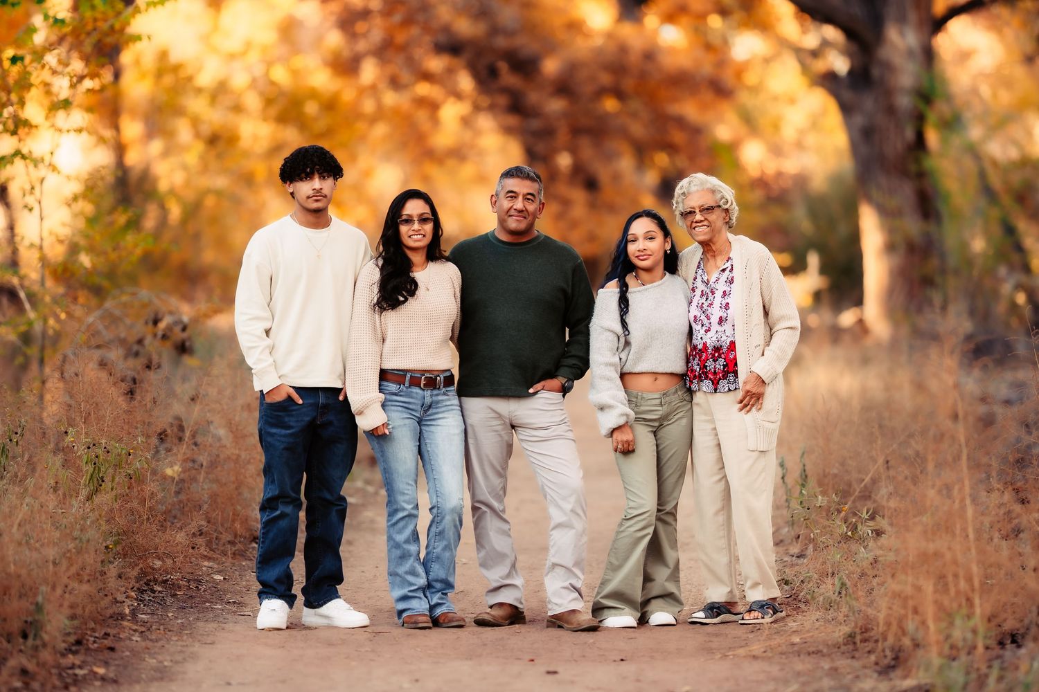 A family sits together on a rustic wooden bench during golden hour in an autumn field.