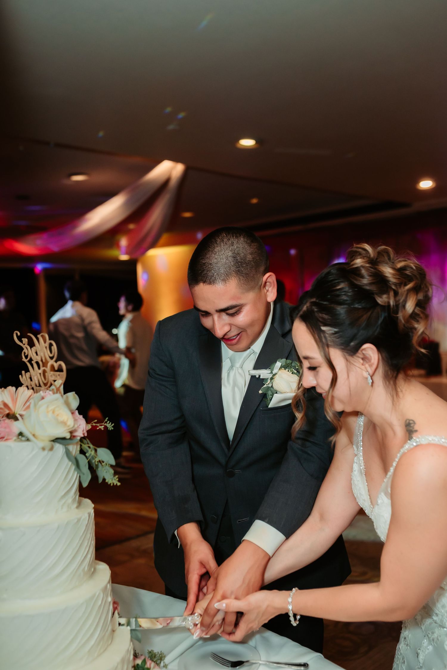 Newlyweds cut their elegant white wedding cake together at their reception celebration.
