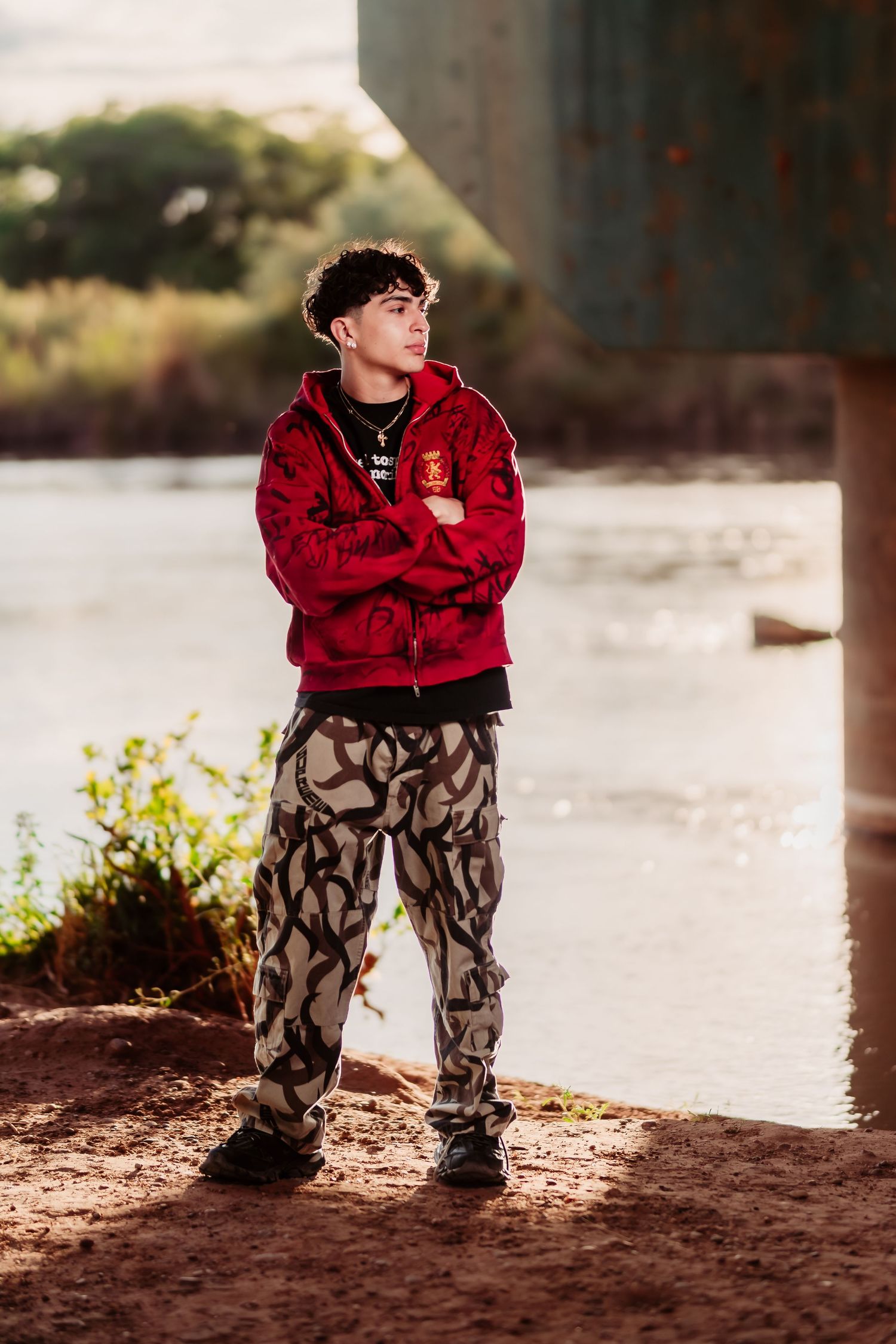 Street style fashion portrait featuring printed pants and red hoodie against a natural outdoor backdrop.