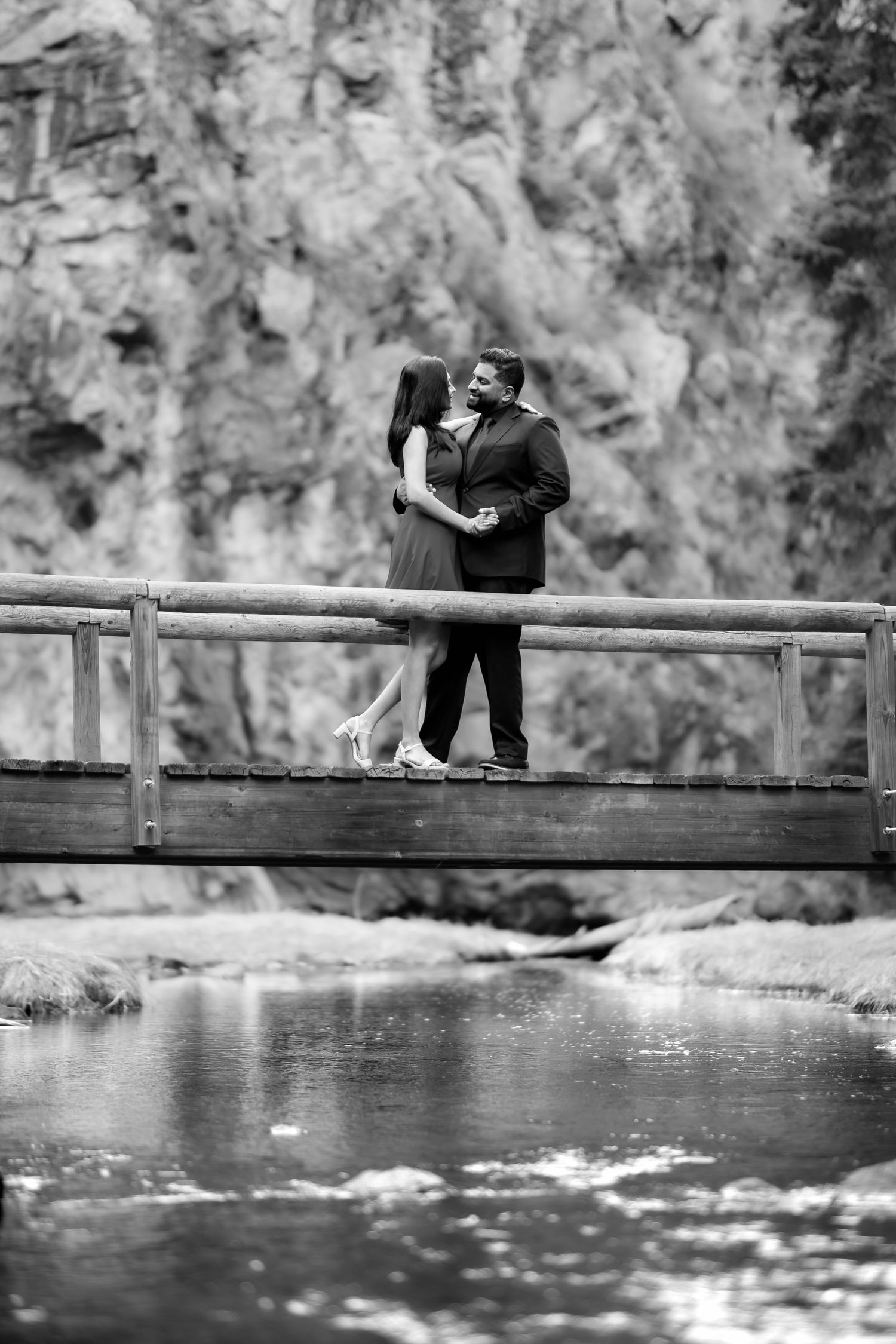 A couple sharing an intimate moment on a wooden footbridge over flowing water.