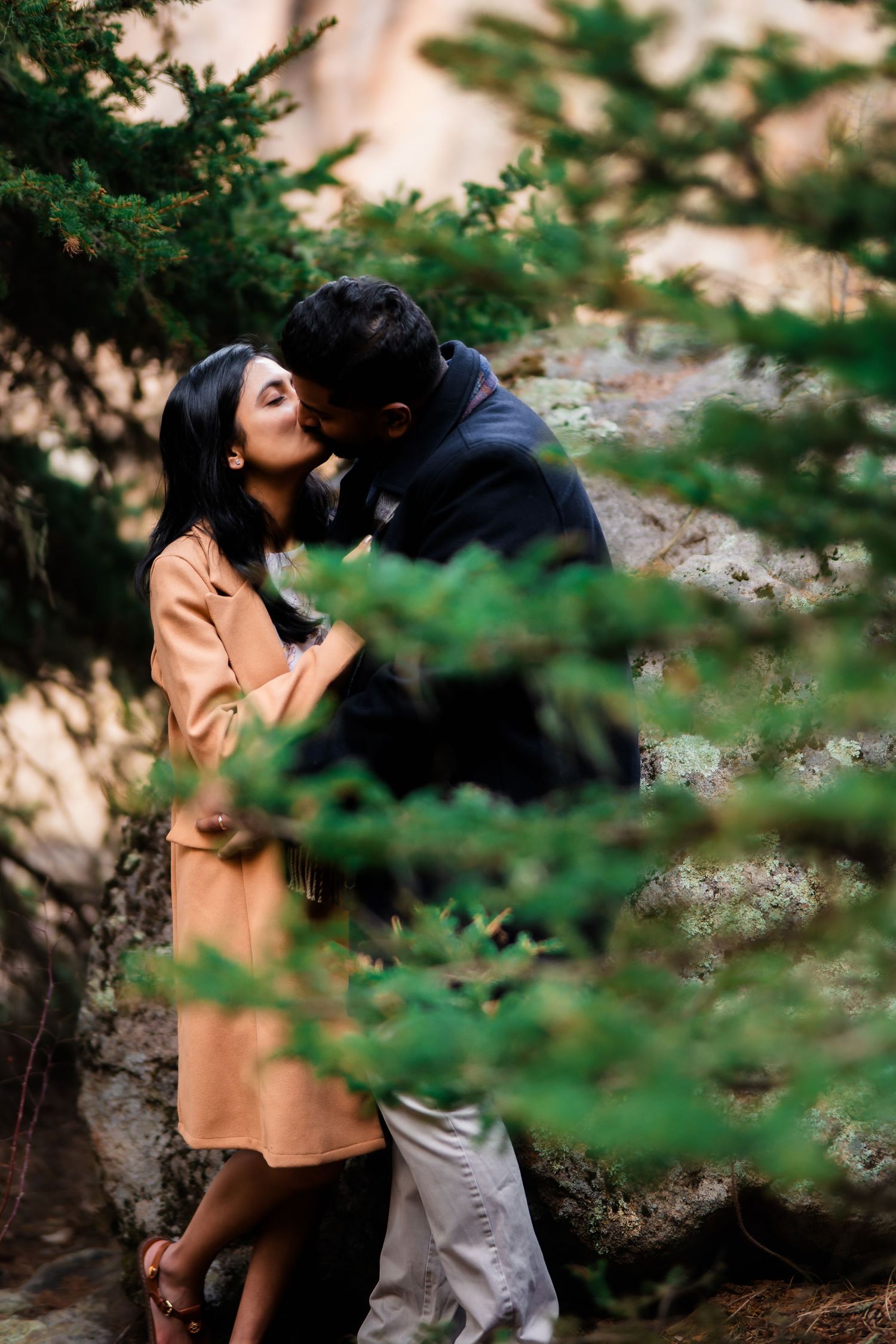 An intimate moment between a couple framed by evergreen branches.