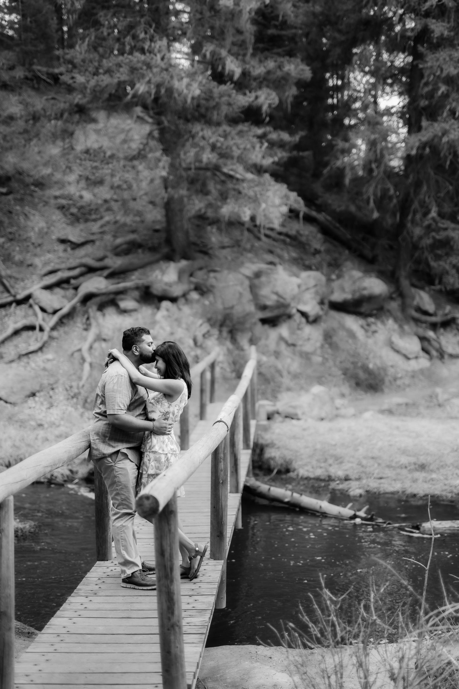 A romantic black and white moment captured on a wooden bridge over water.