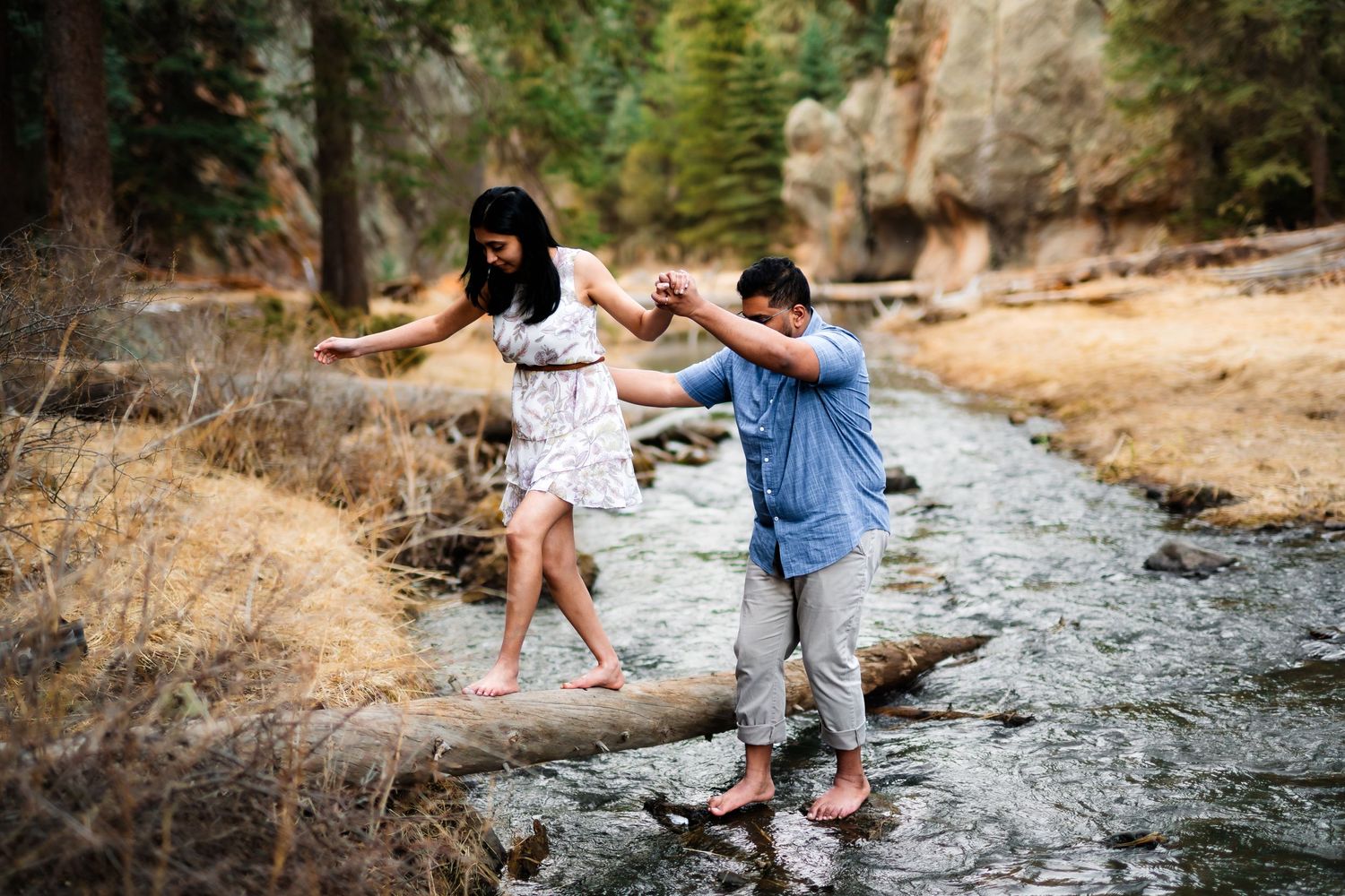 A couple carefully crosses stepping stones over a mountain stream together.