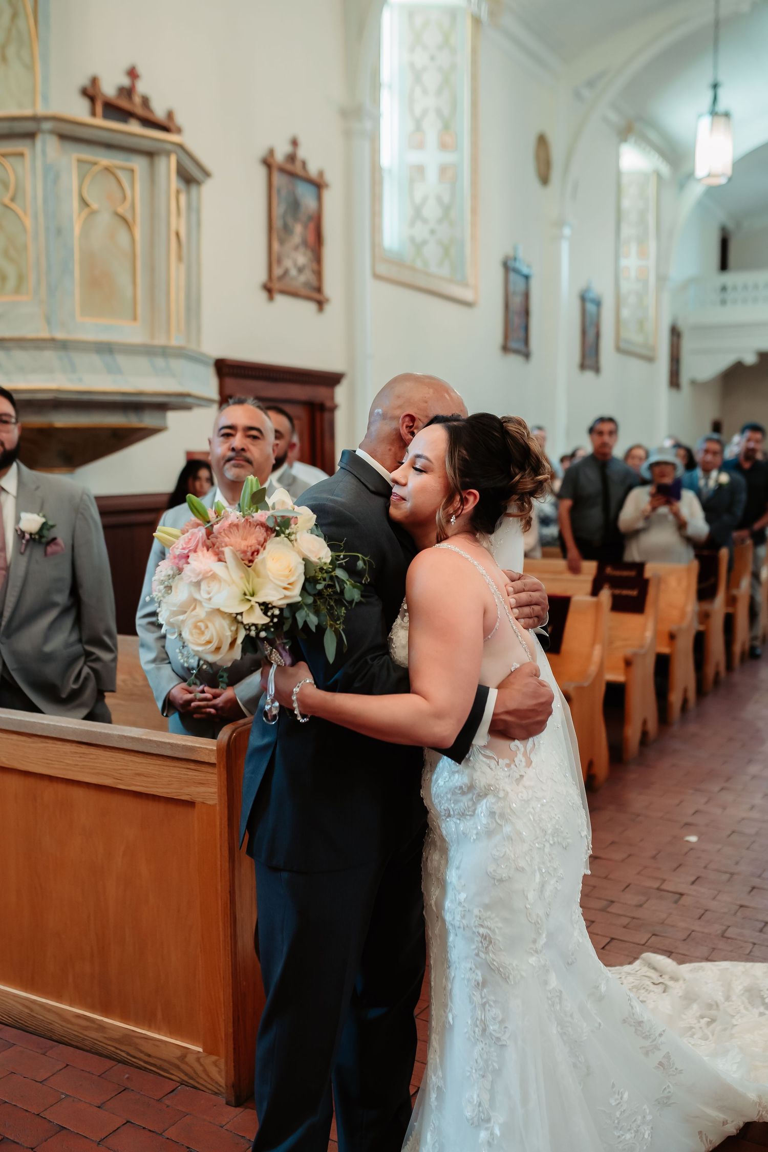 Wedding attendees embrace in emotional moment inside traditional church setting.