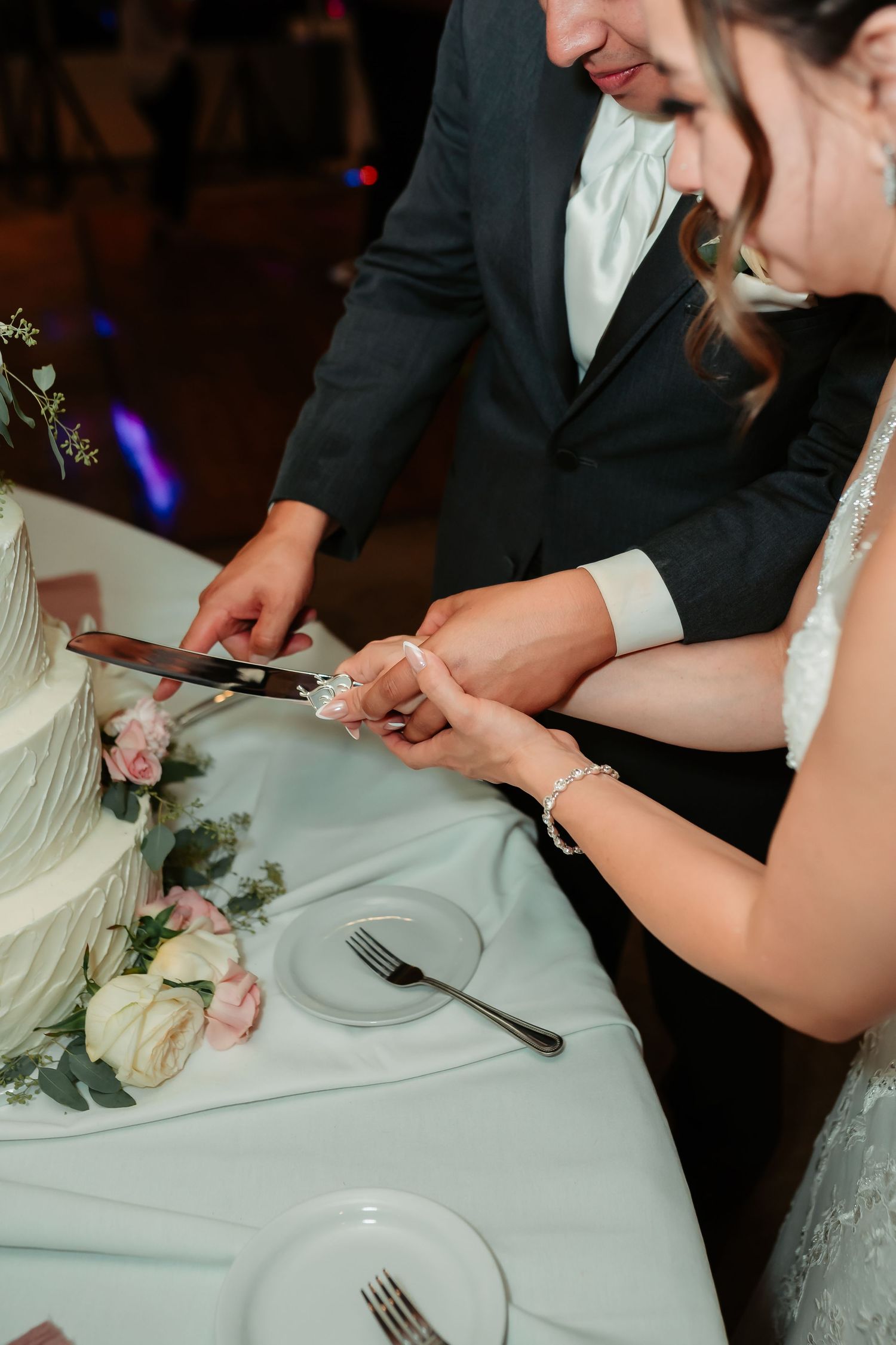A couple cuts their wedding cake decorated with fresh flowers at the reception.