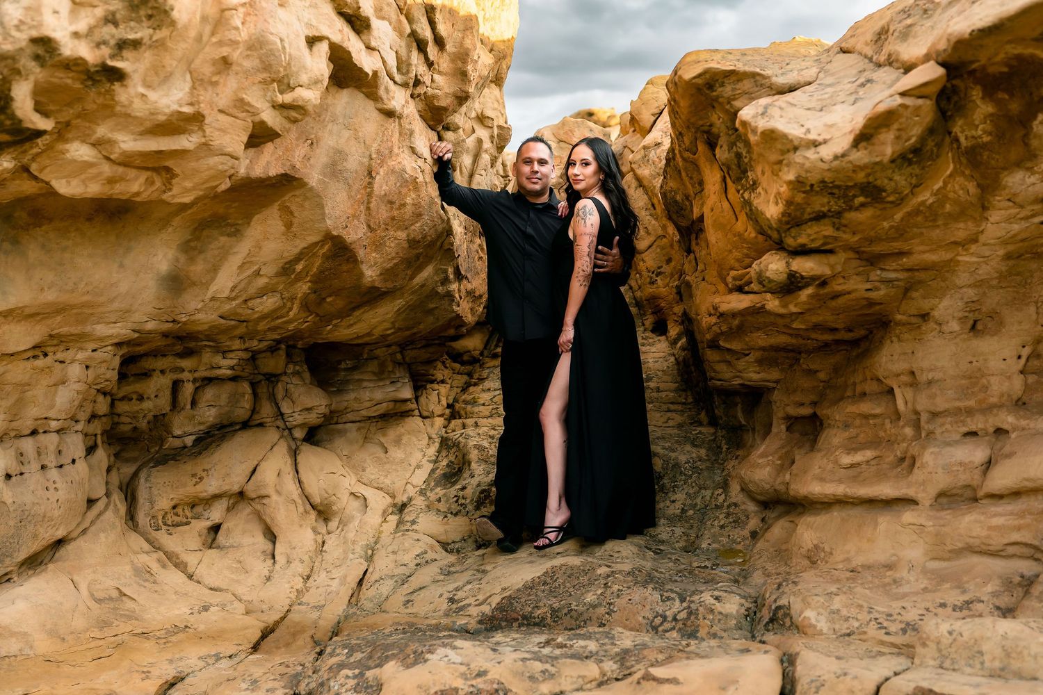Two women in elegant black gowns posing among golden sandstone rock formations.