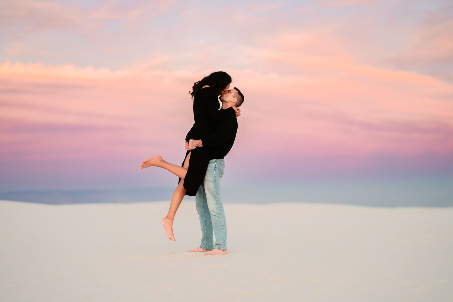 Silhouetted figure stands against a pastel pink and purple sunset sky with outstretched arms.