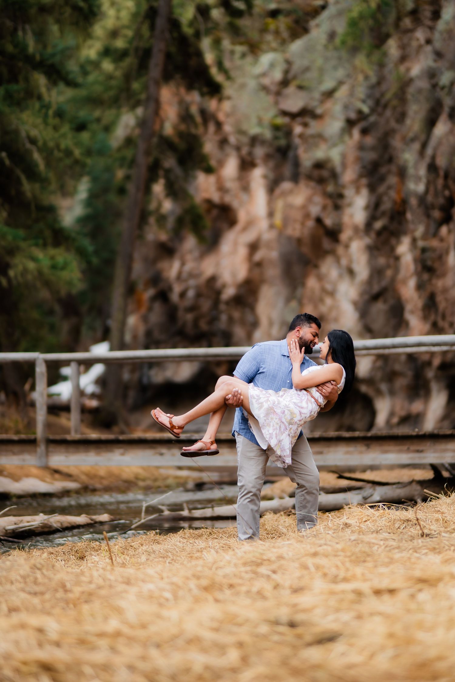 A romantic couple embraces in a passionate dip pose against a scenic rocky cliff backdrop in nature.