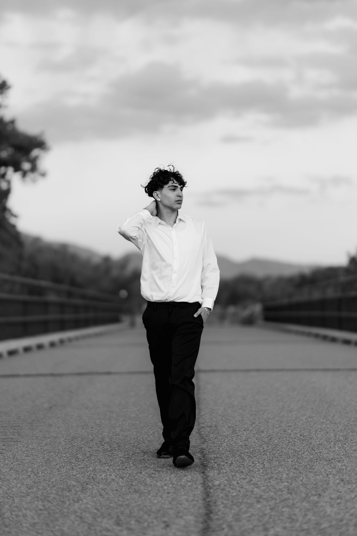 A person in a white shirt and dark pants walks alone on a bridge in black and white photography.