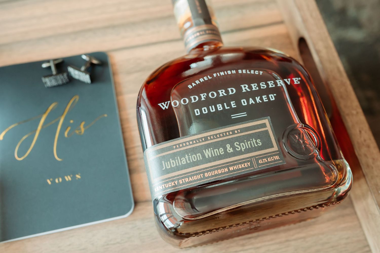 Several bottles of Woodford Reserve bourbon whiskey displayed alongside blue wedding stationery on a wooden surface.
