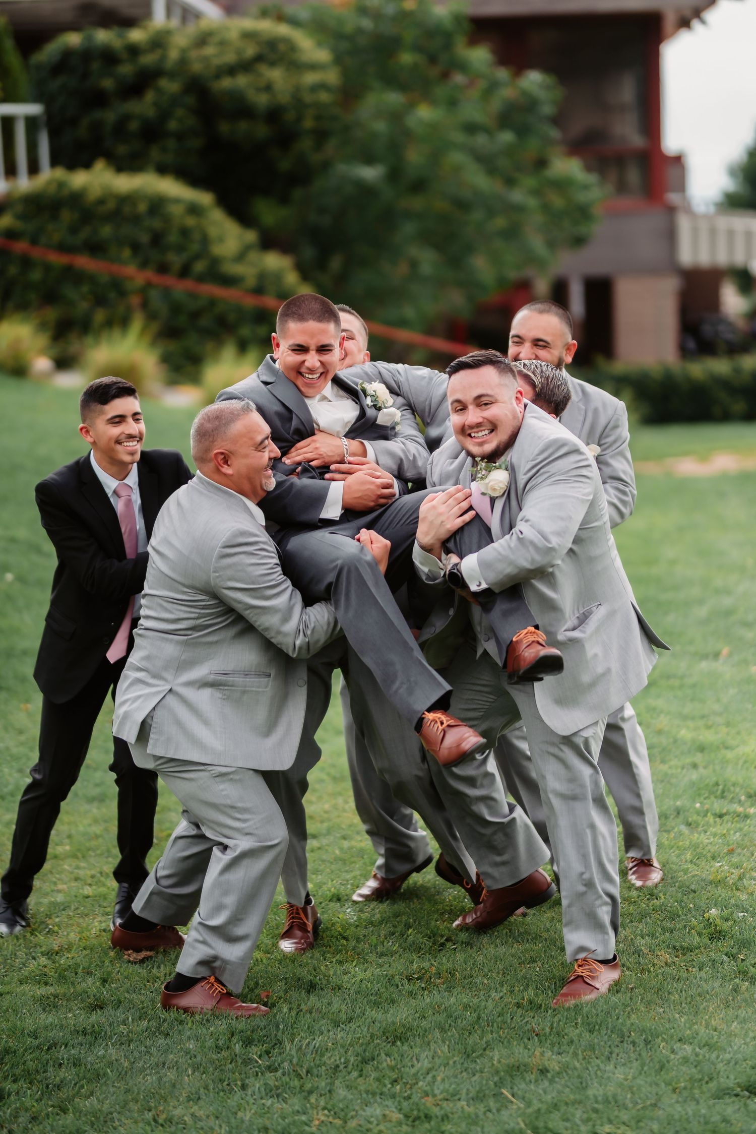 Groomsmen in matching gray suits pose energetically in a line formation during outdoor wedding photos.
