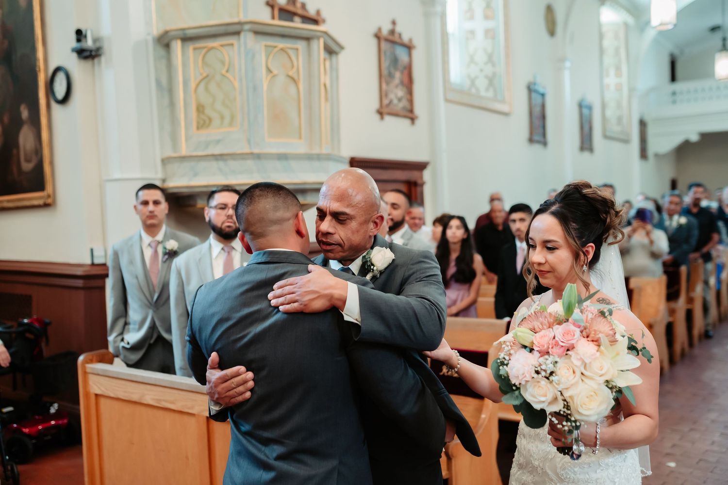 Wedding ceremony guests exchanging hugs in ornate church interior.