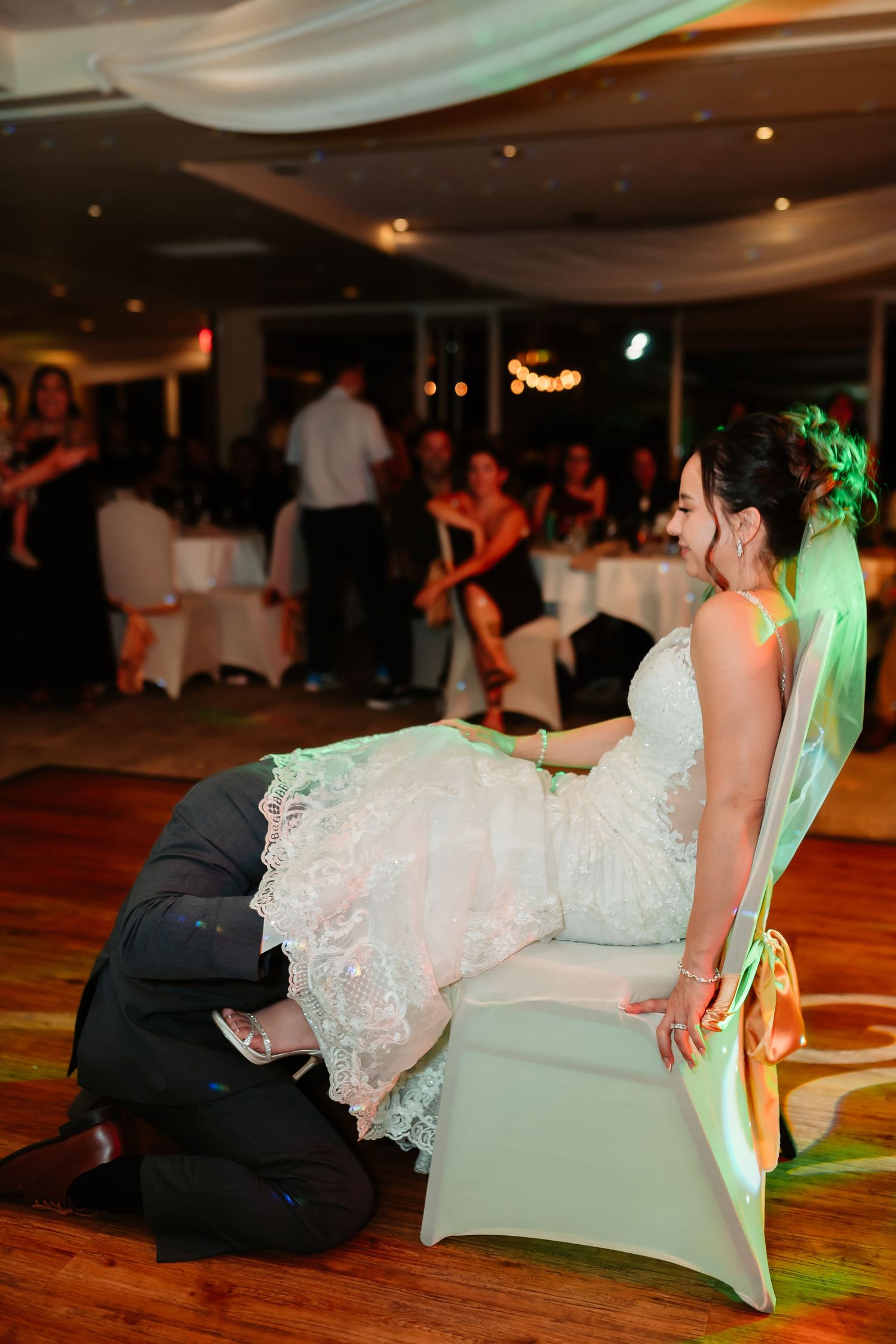 Wedding couple performs a playful reception dance move on the floor with guests watching in the background.
