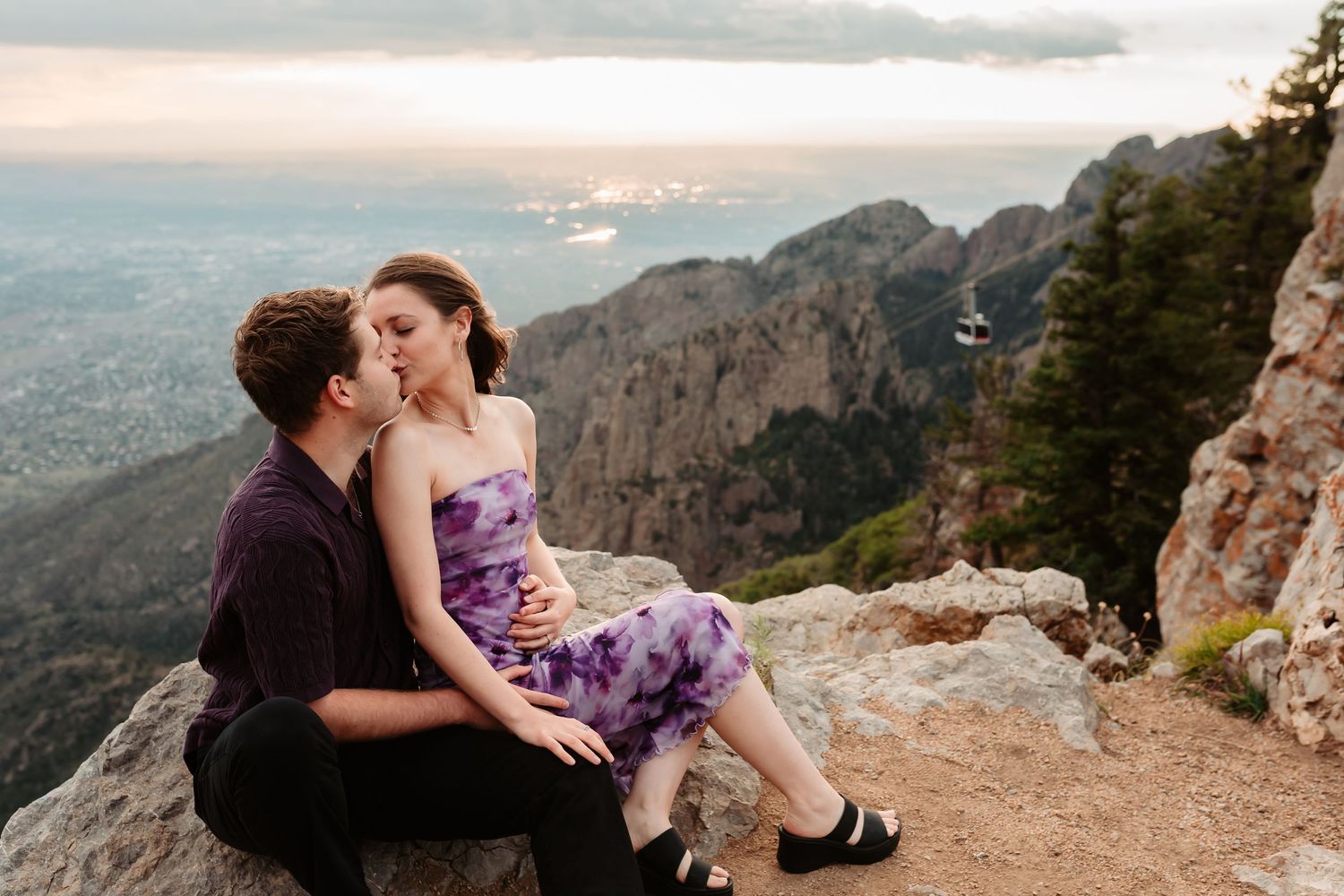 Intimate couple moment captured on scenic mountain cliff edge during sunset with panoramic landscape views.