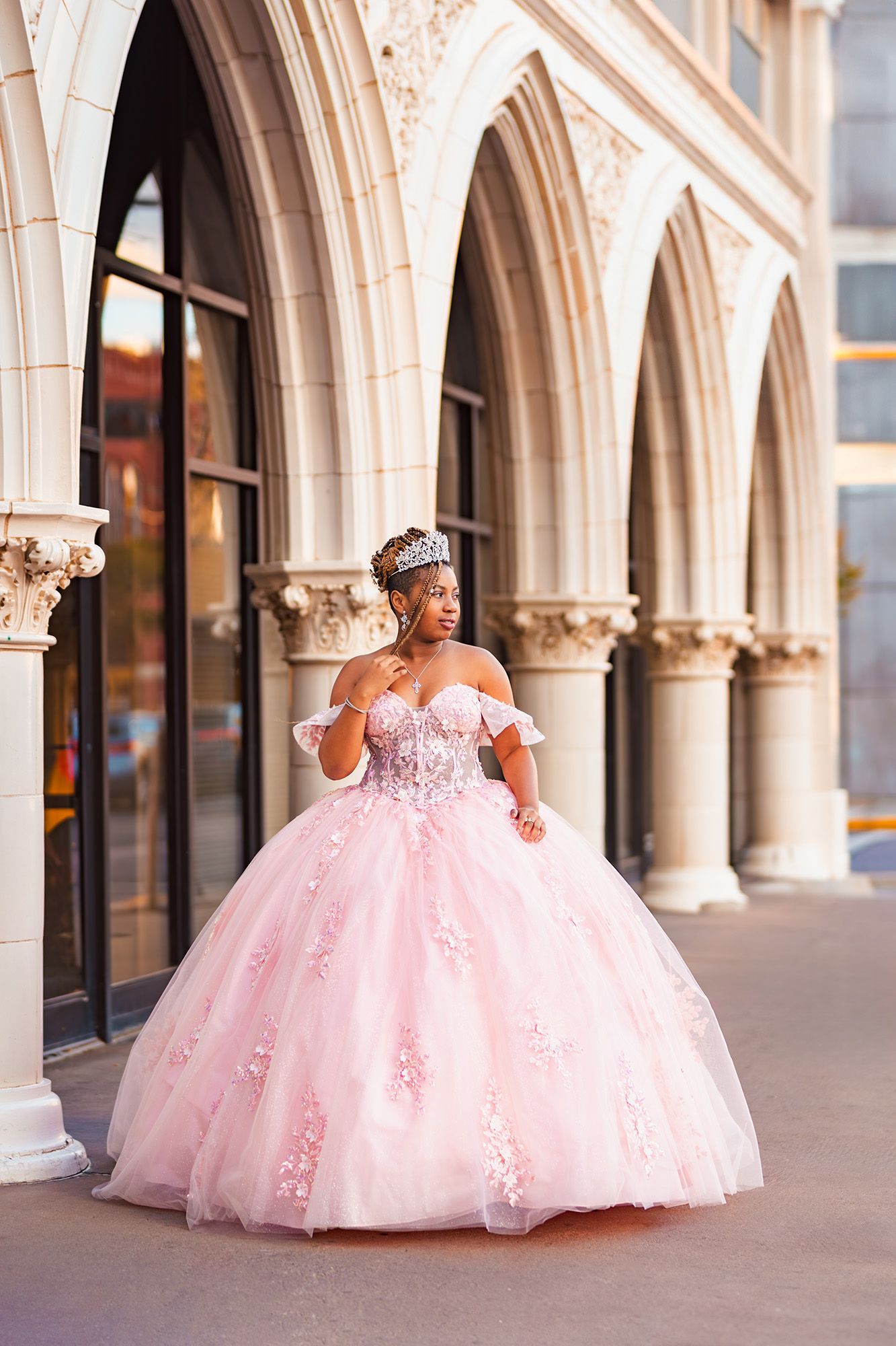 Elegant pink ballgown dress with lace details photographed in a classic arched colonnade setting.