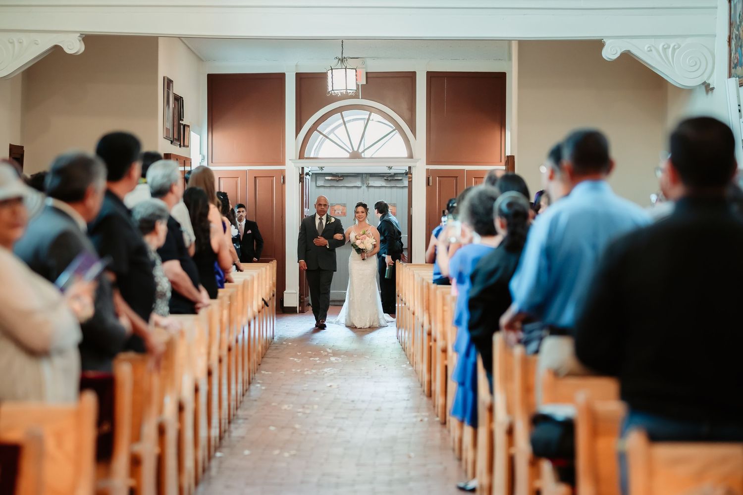 A couple stands at the altar during their wedding ceremony inside a traditional church with guests seated in wooden pews.