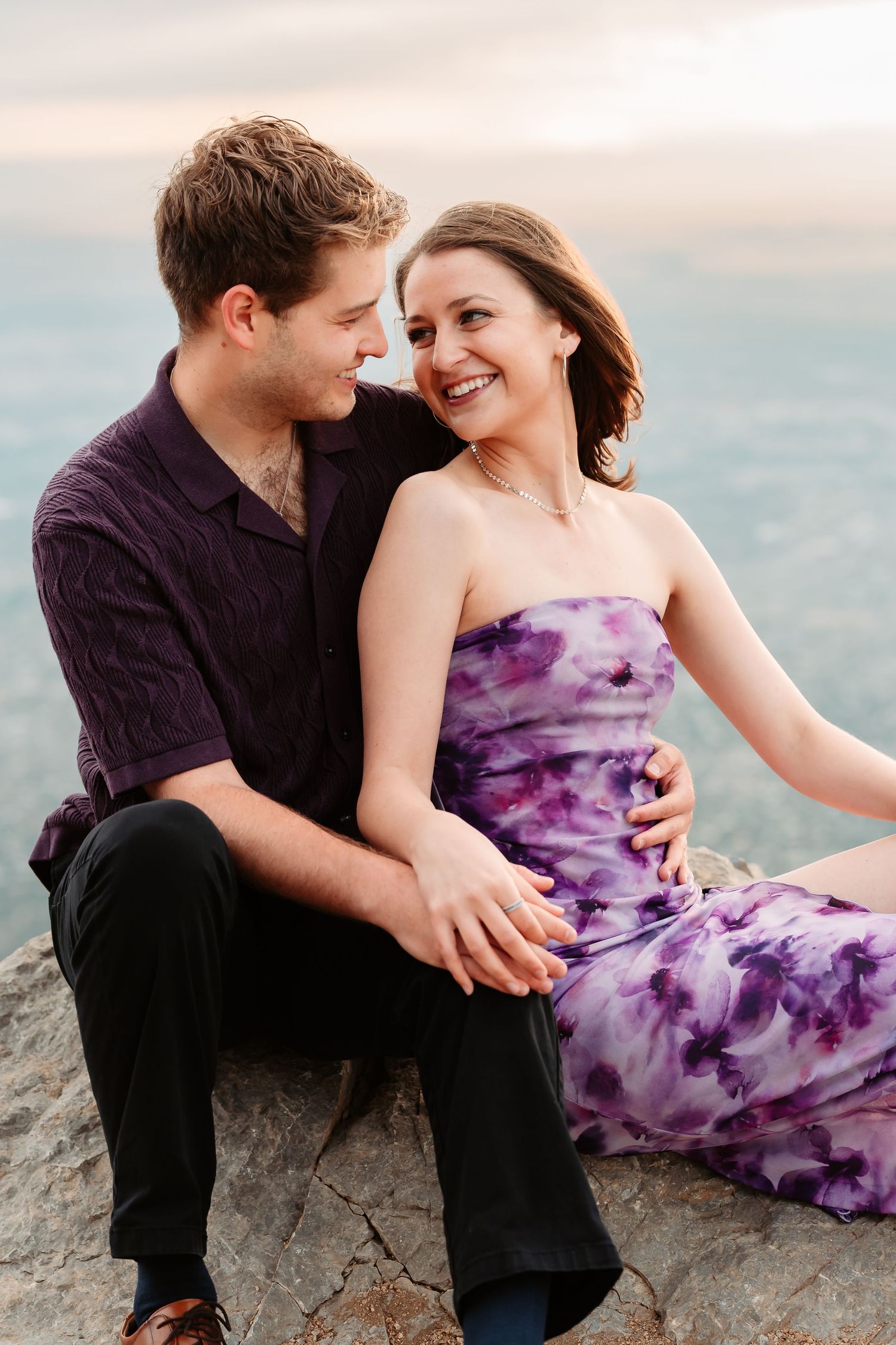 A couple in casual attire sharing intimate moments on rocky mountain terrain at dusk.