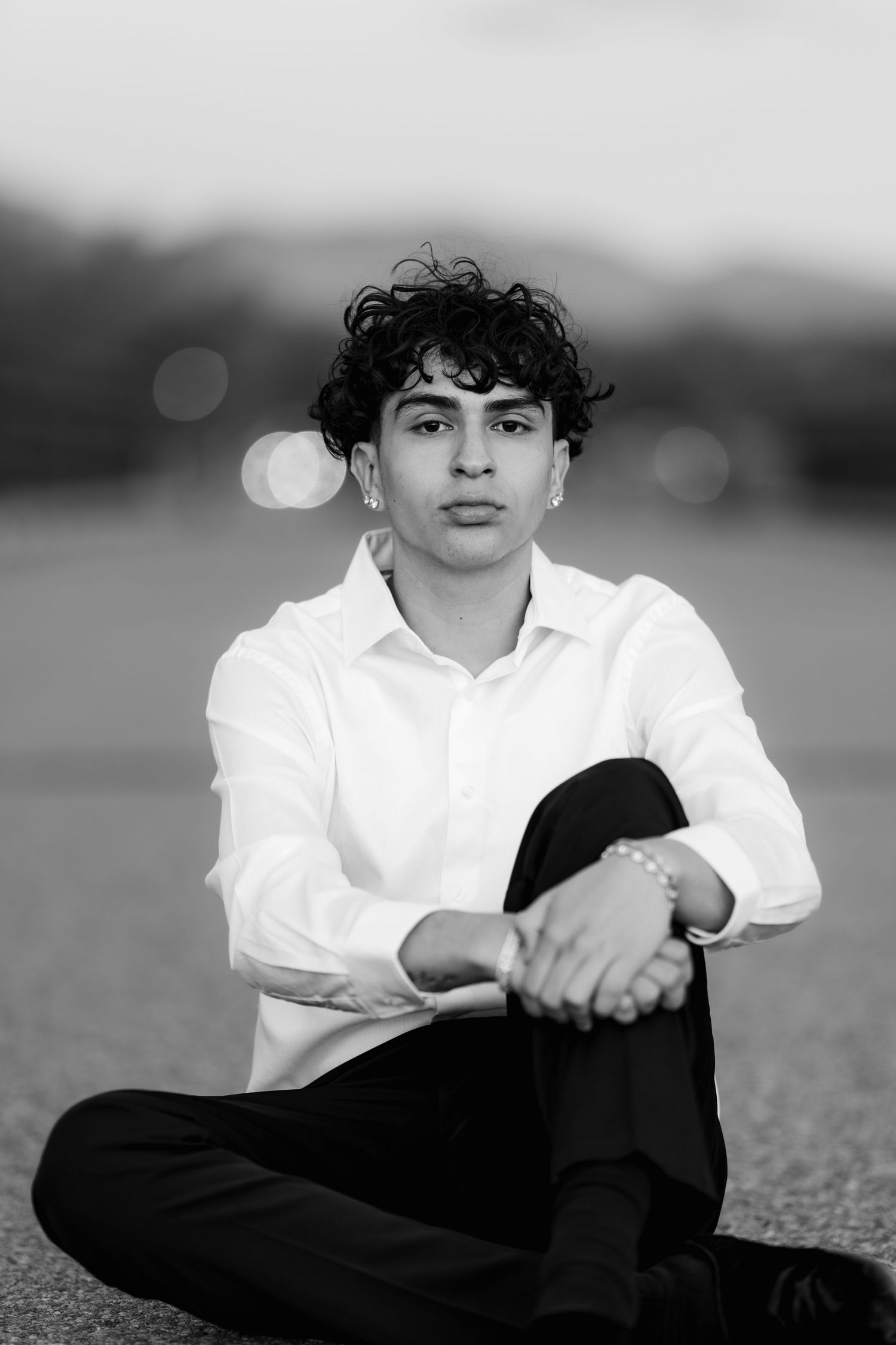 Black and white portrait of person in white dress shirt sitting cross-legged outdoors.