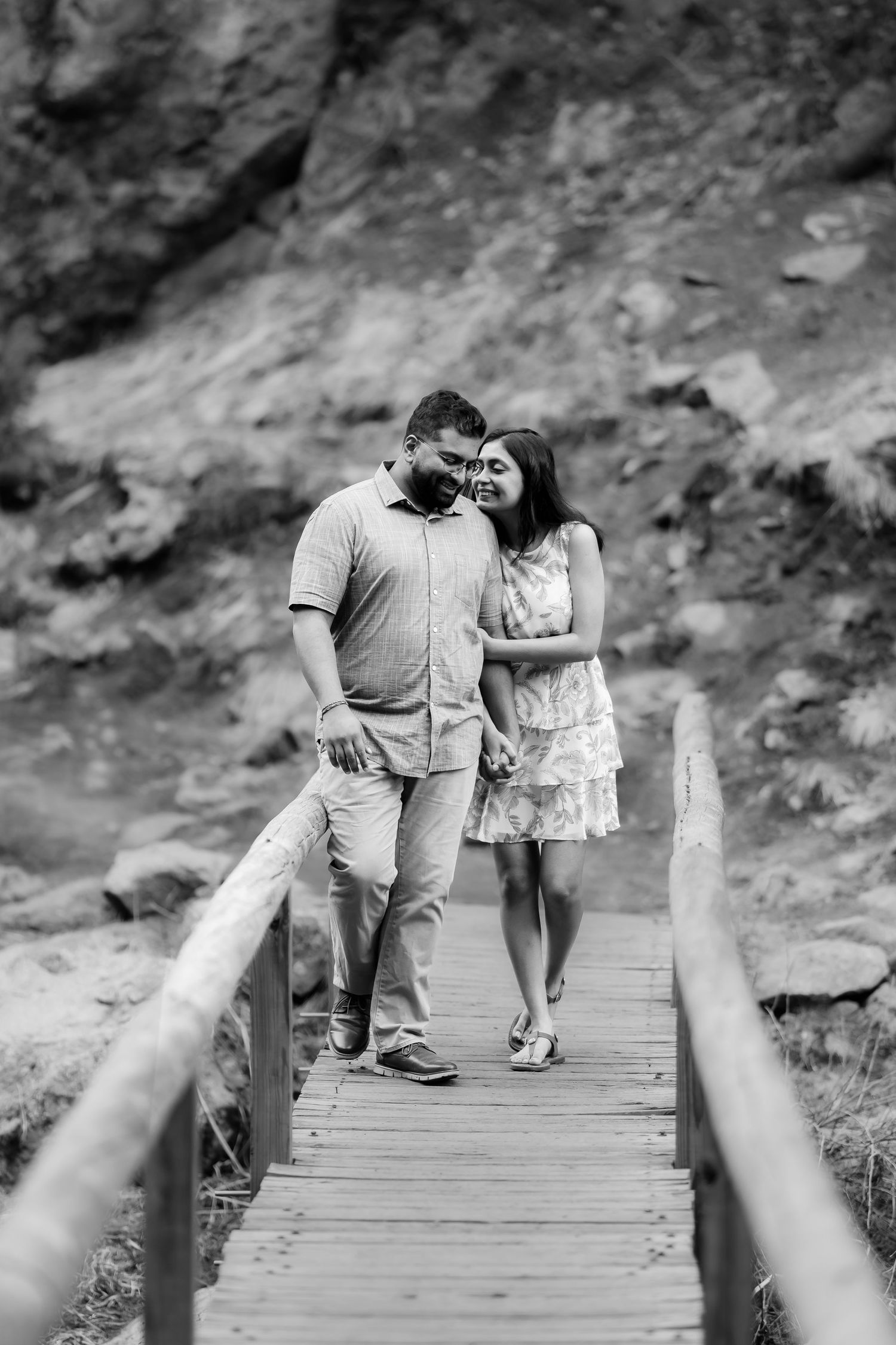 A couple shares an intimate moment while walking on a wooden boardwalk surrounded by rocky terrain.