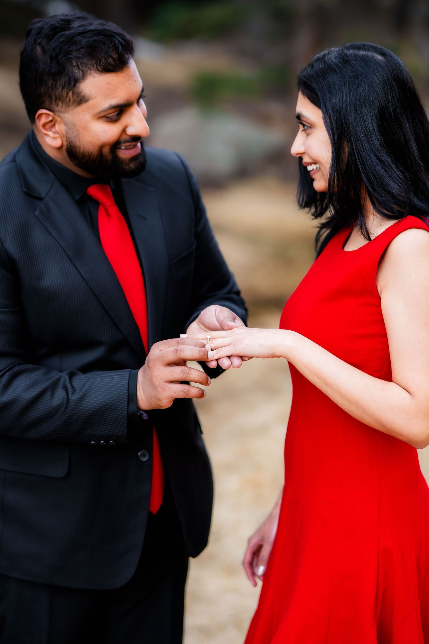 A couple in formal red and black attire sharing an intimate moment during an outdoor engagement photo session.