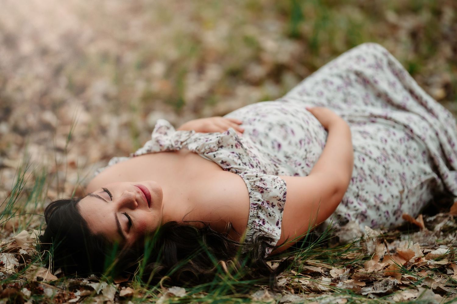 A person in a floral dress lying on the ground among autumn leaves and grass.