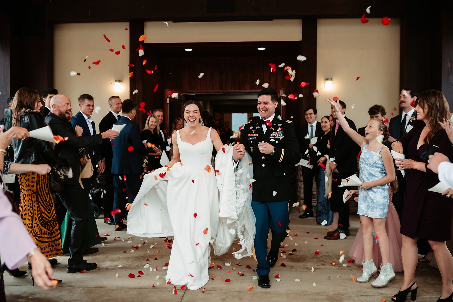 Bride and groom exit wedding ceremony through cheering guests tossing colorful flower petals in joyful celebration.