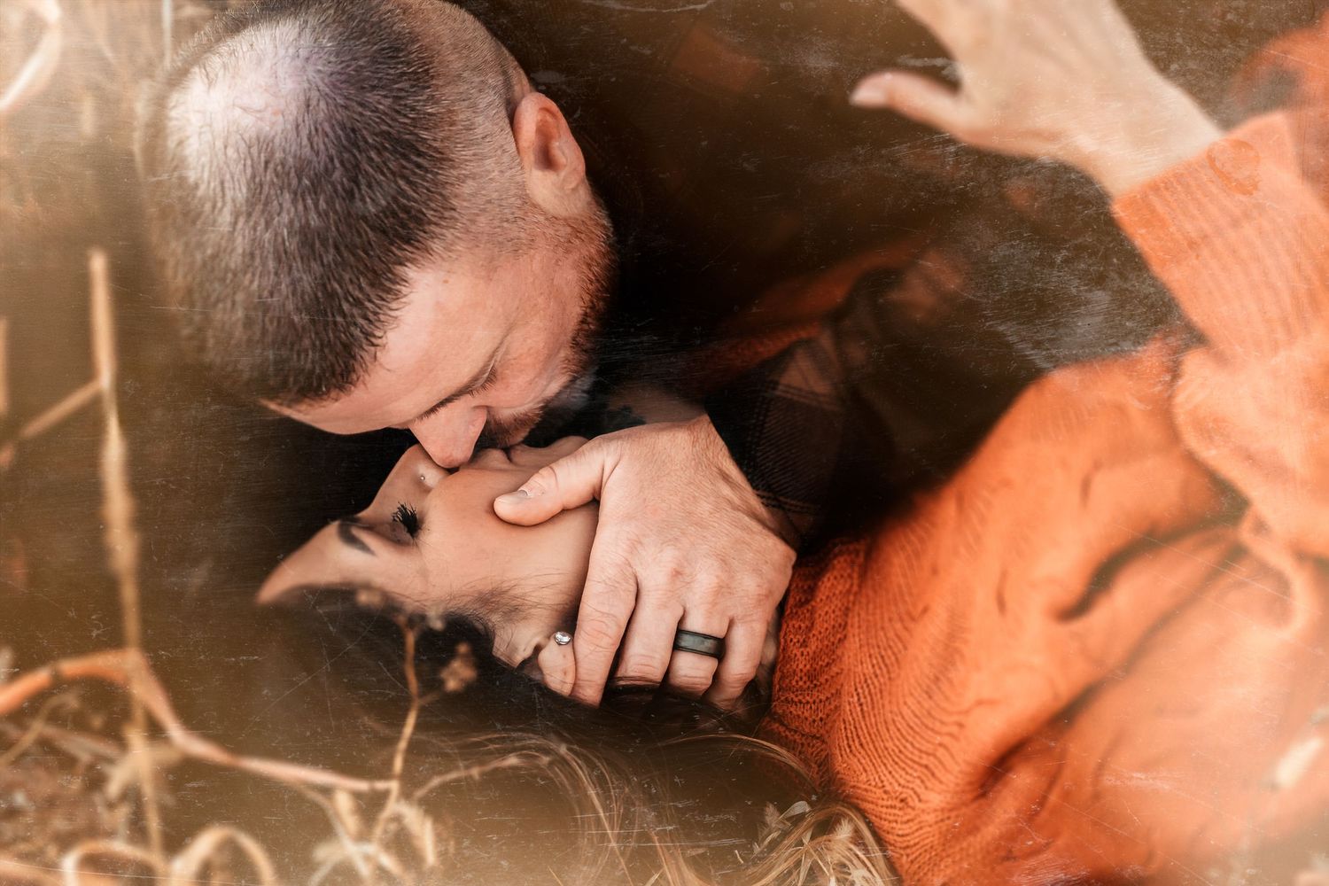 A tender moment between two people lying in grass, one wearing an orange sweater.
