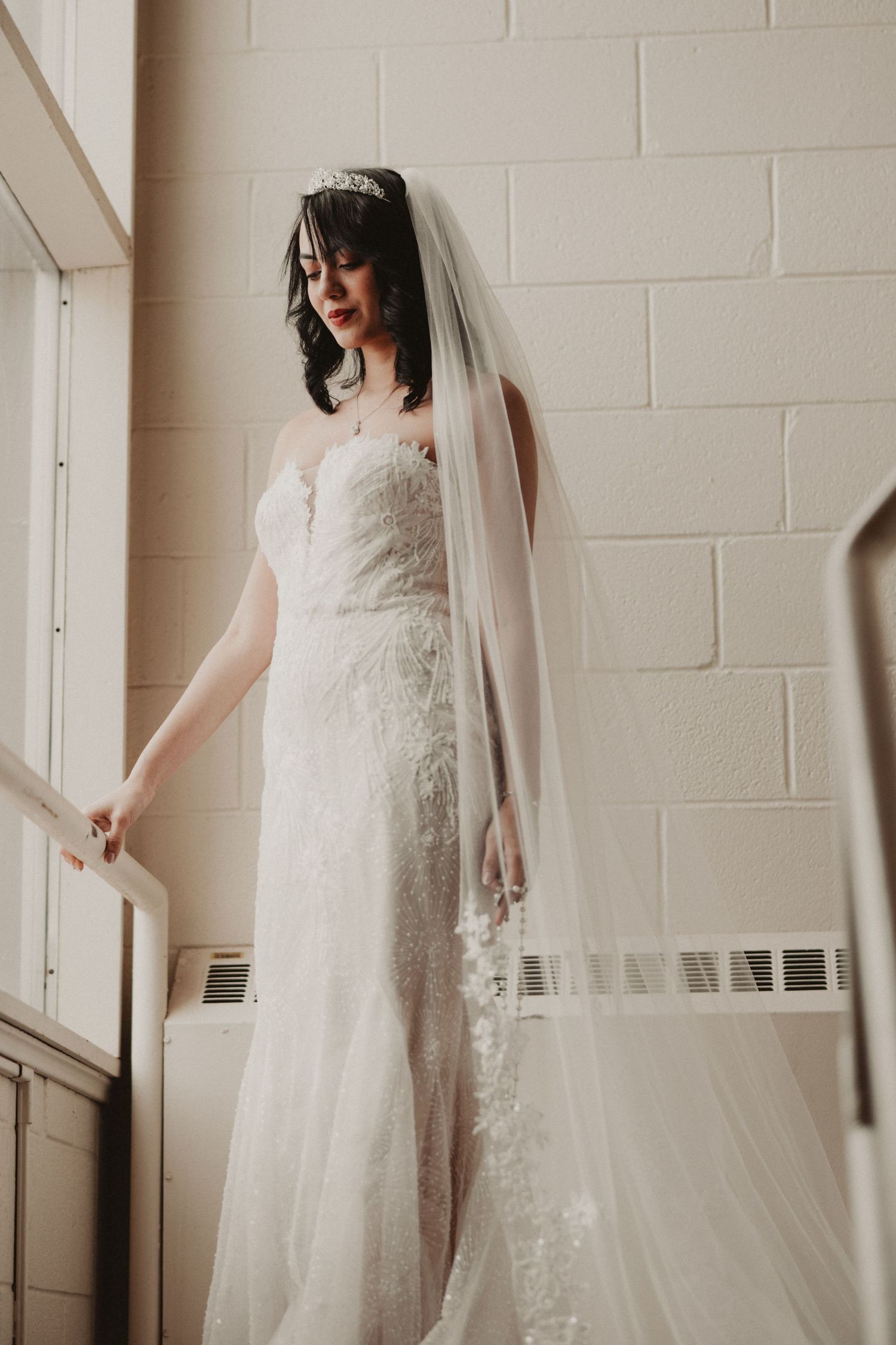 A series of bridal portraits showing an elegant lace wedding dress and long veil against a white brick wall.