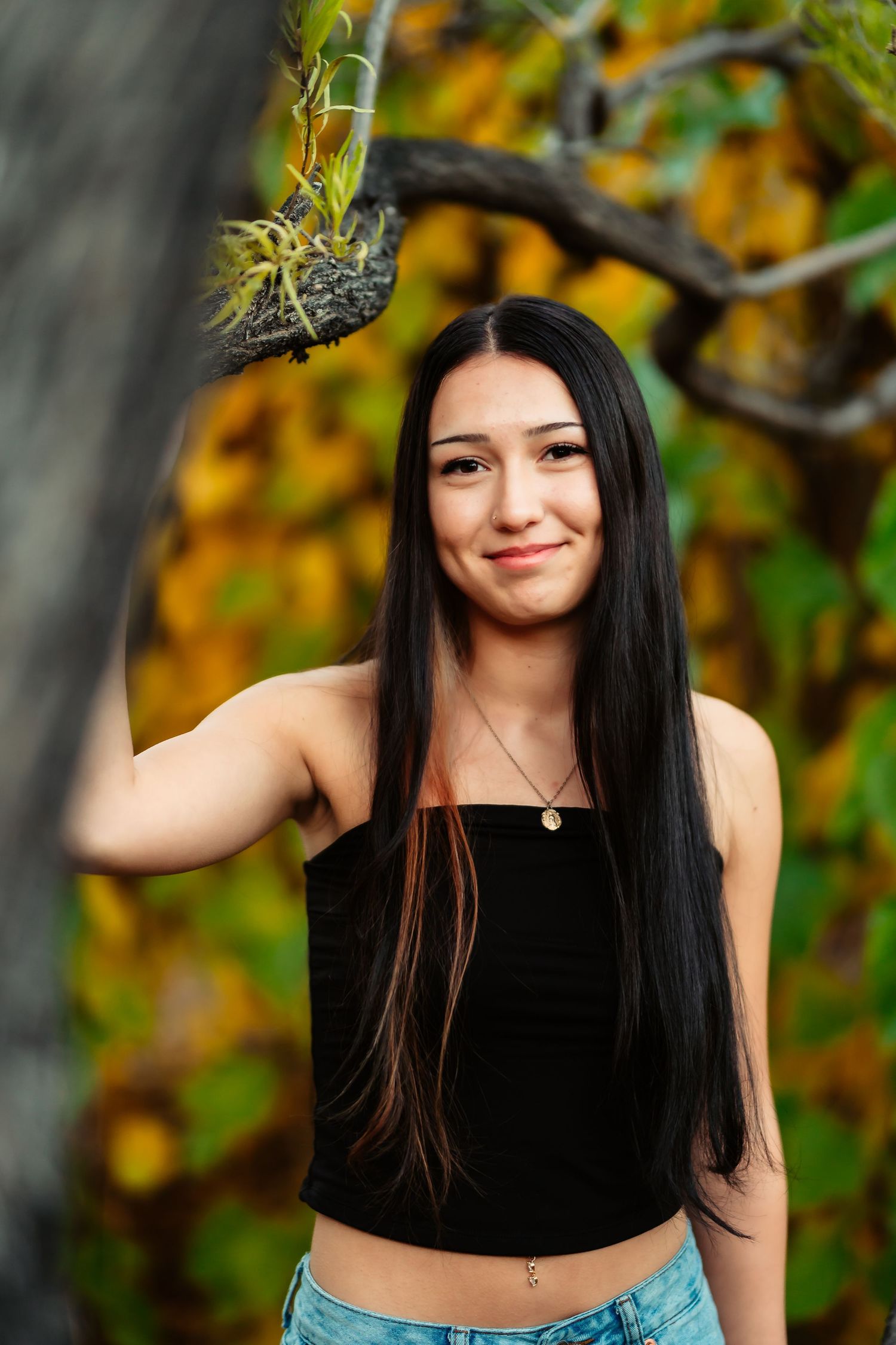 Portrait of someone in a black crop top and long dark hair against autumn foliage in soft focus.