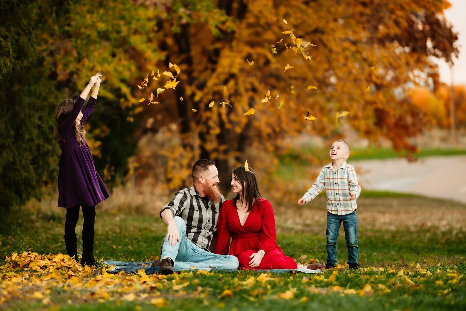 A couple enjoys a romantic autumn picnic surrounded by golden fallen leaves in a park setting.