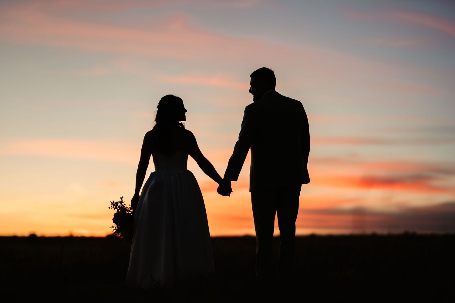 Silhouettes of people walking together against a vibrant orange and pink sunset sky.