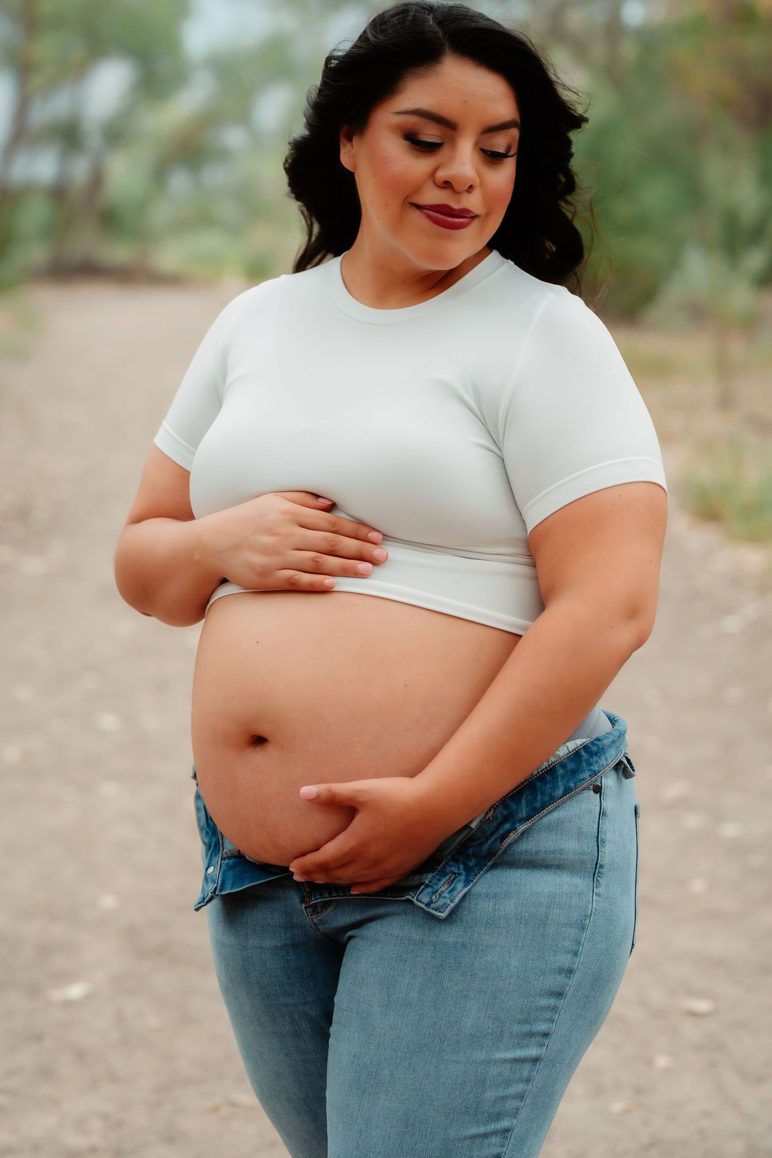 A series of photos showing a person in a white t-shirt and jeans gently cradling their stomach in a natural outdoor setting.