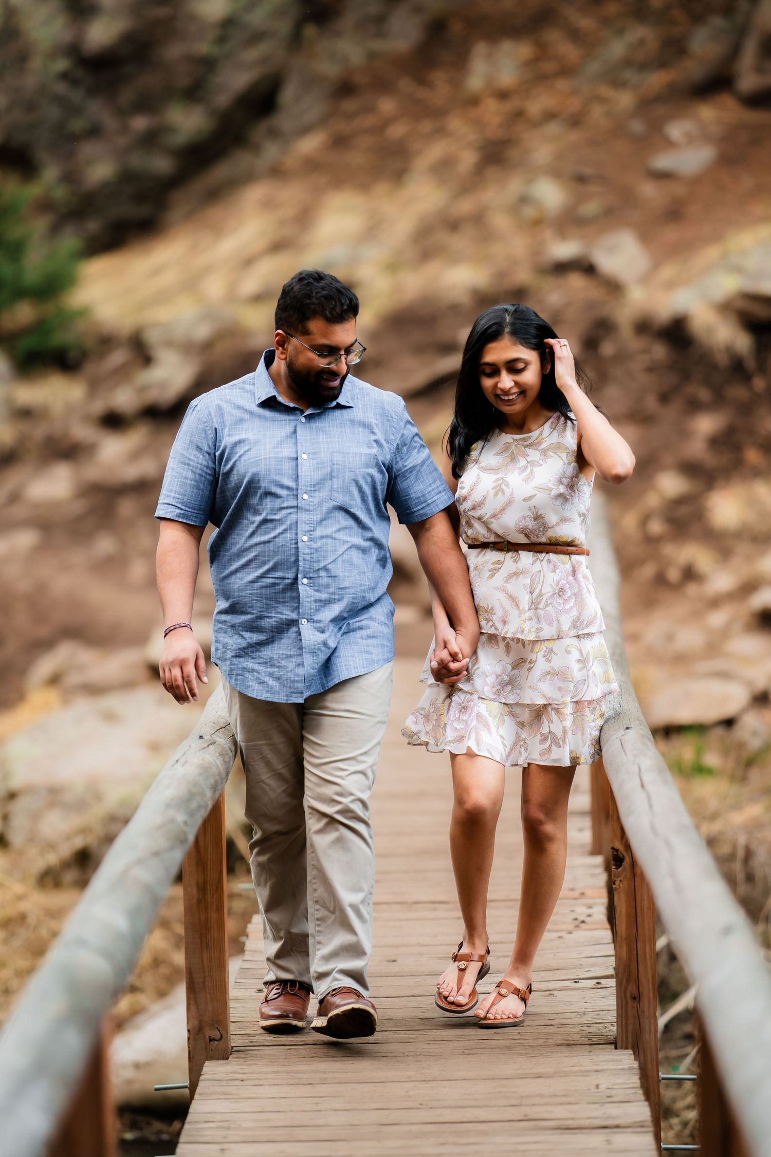 A couple walks hand in hand across a wooden bridge surrounded by natural scenery.