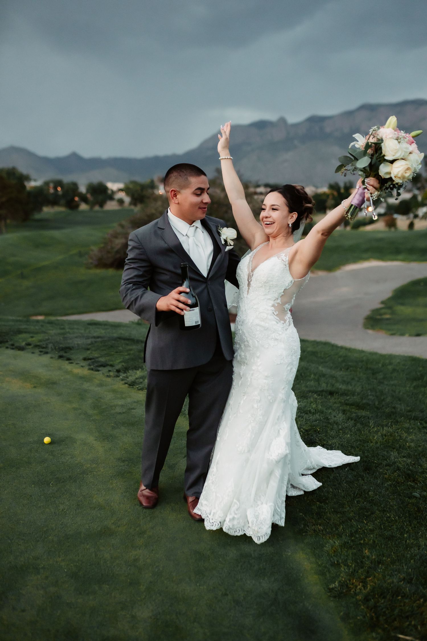 Celebratory moment of newlyweds dancing on golf course with mountains in background.