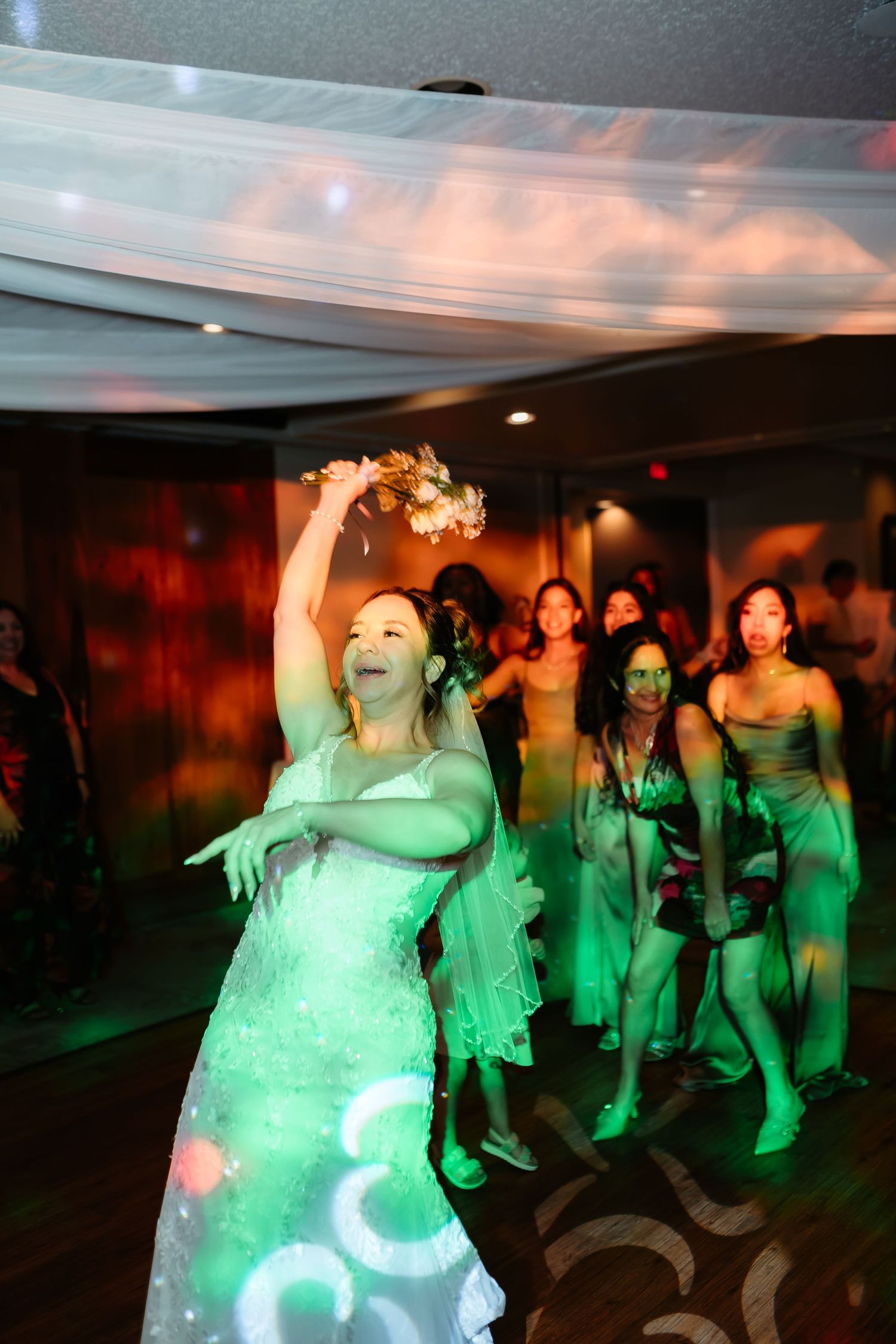 Wedding reception dancers illuminated by green lighting enjoy the celebration on a dimly lit dance floor.