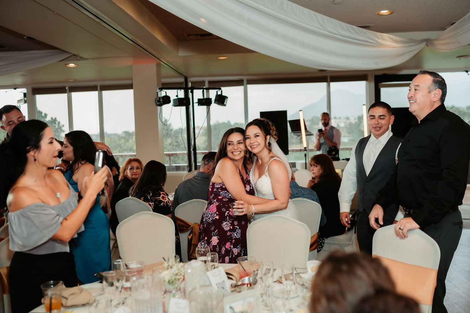 Guests celebrate at an elegant reception venue with white tablecloths and draped fabric ceiling decor.