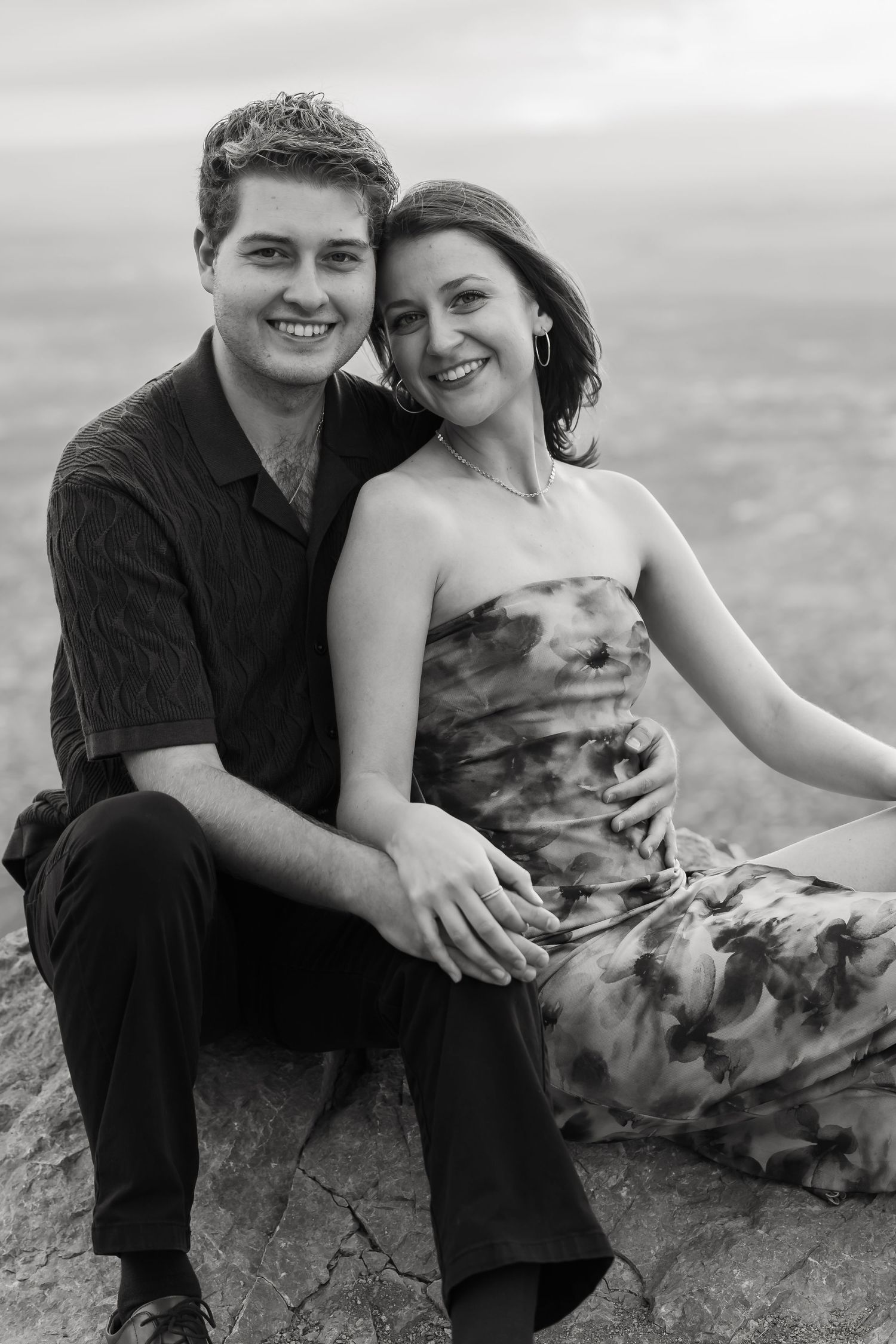 Black and white romantic portraits of a couple sitting together on a mountain overlook.