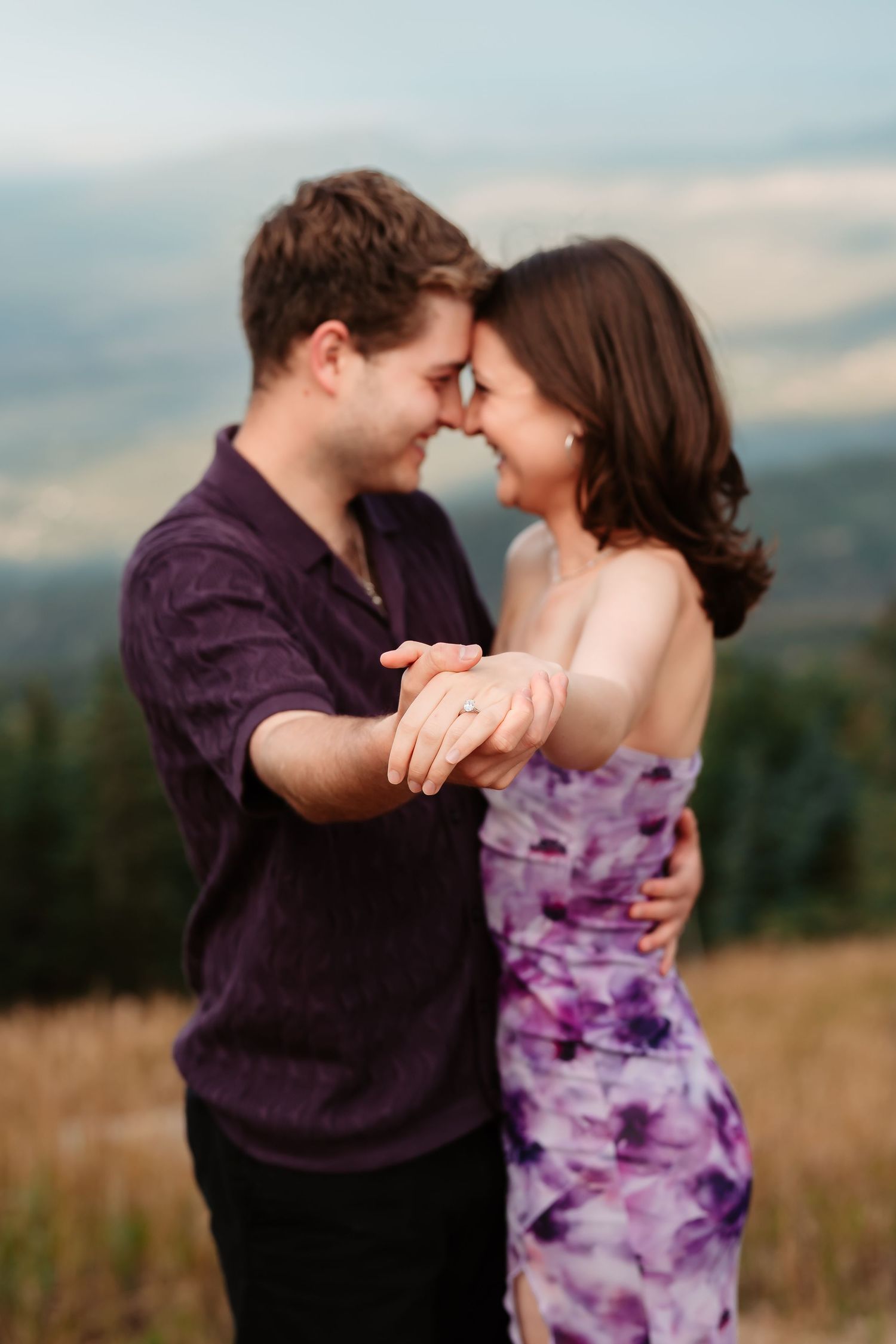 A couple shares intimate moments in a field with mountains in the background.