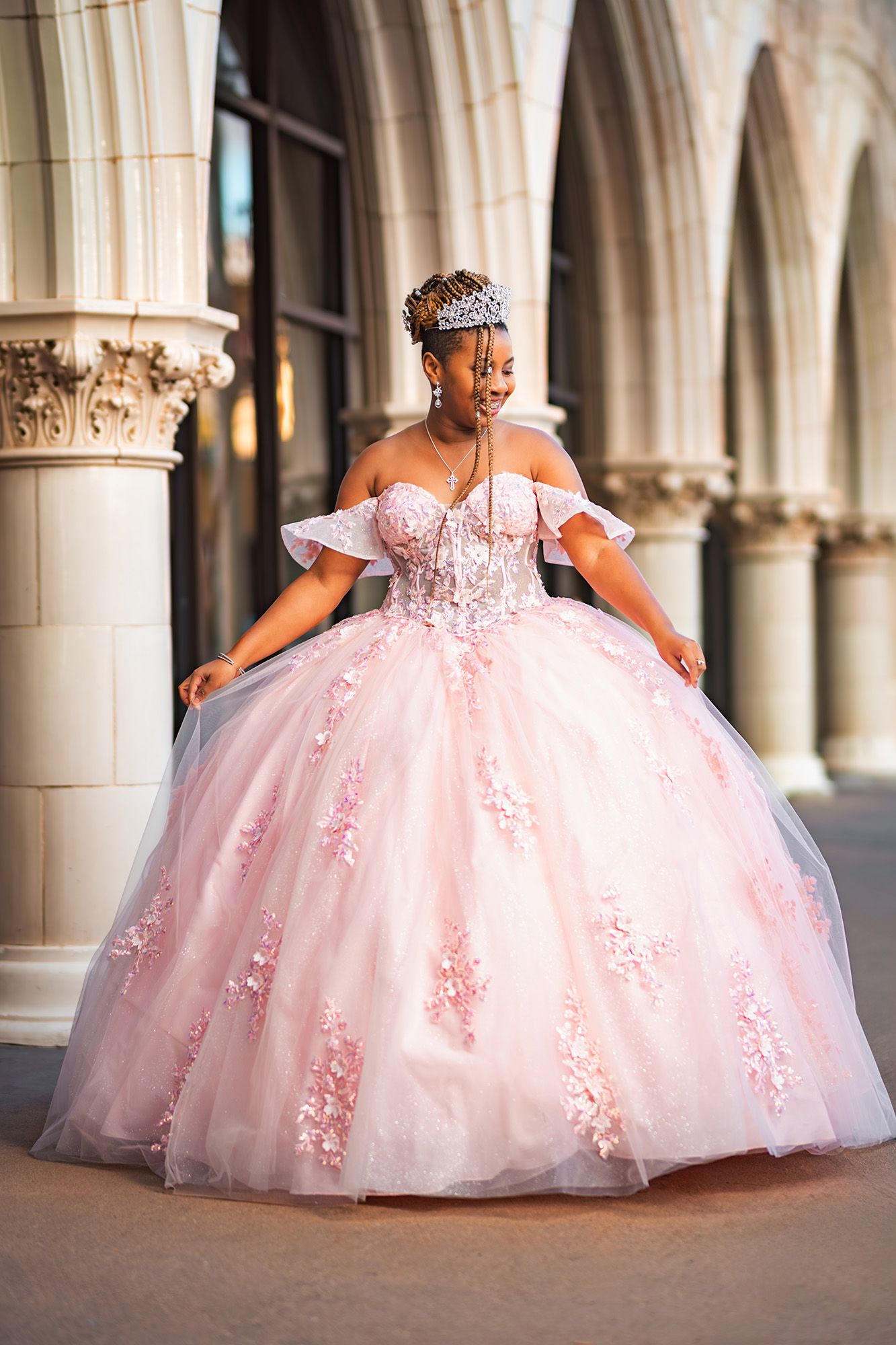A stunning pink ball gown with off-shoulder sleeves and floral lace details photographed in an elegant archway setting.