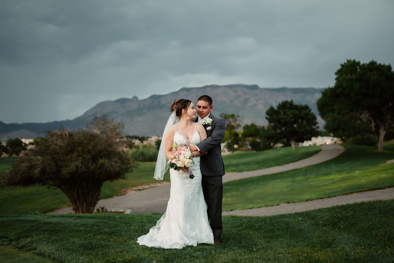 Wide angle shot of wedding couple embracing on golf course with mountain vista.