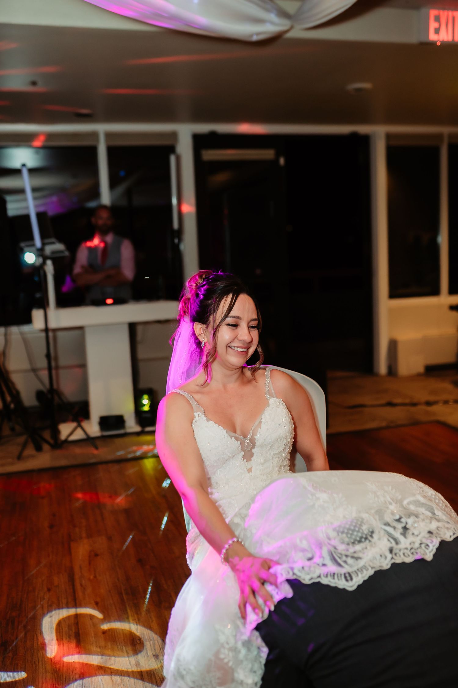 Bride in white lace dress dips down during a festive dance at wedding reception.
