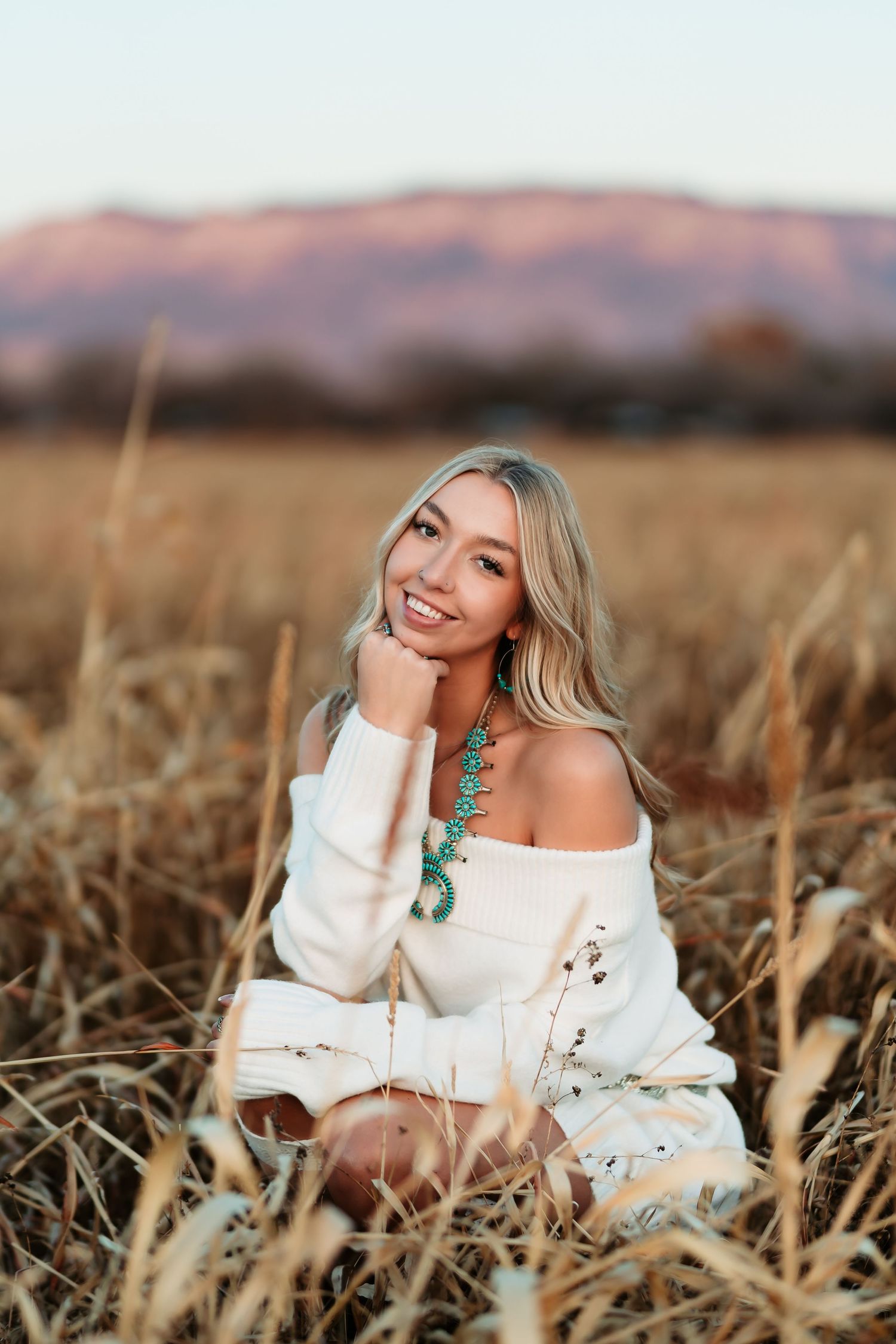 Portrait in a golden wheat field at sunset wearing a white sweater and turquoise statement necklace.