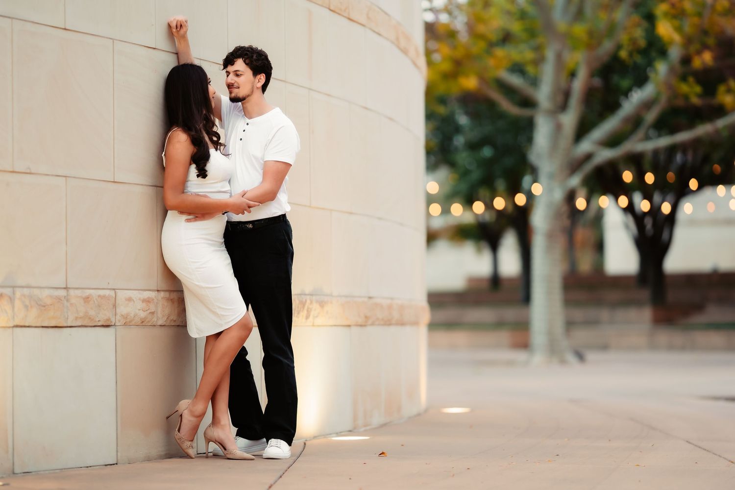 A couple embraces against a stone pillar during an outdoor photo session at golden hour.