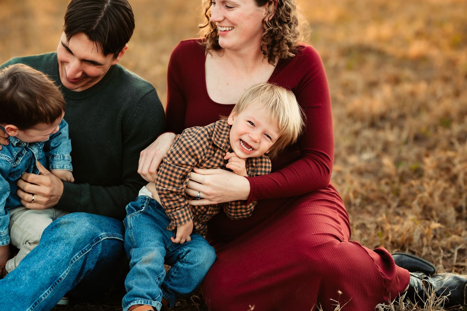 A loving family shares joyful laughter while sitting together in a golden autumn field at sunset.