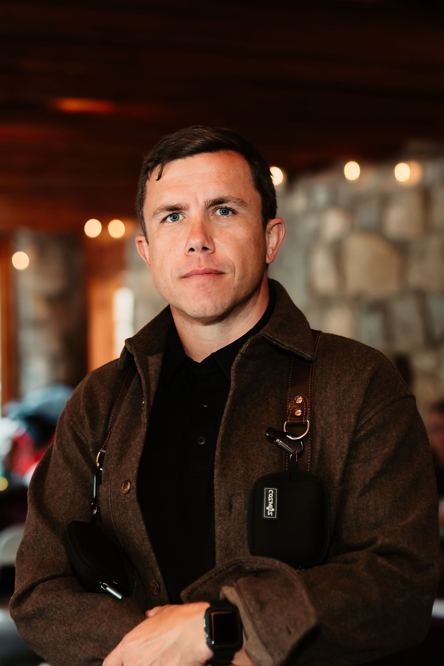 A person in a brown jacket sits at a restaurant table with warm lighting and blurred background in view.
