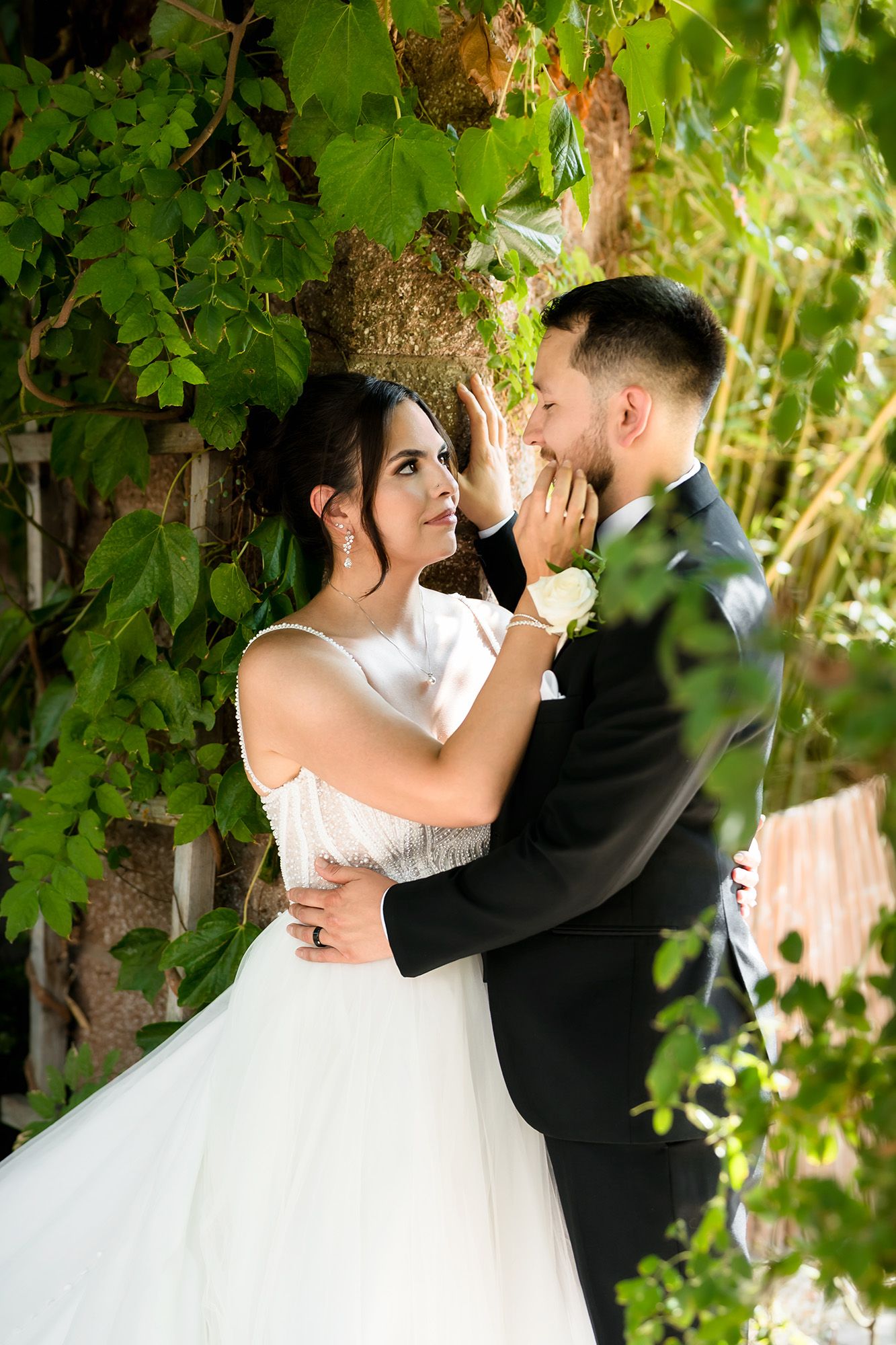 Bride and groom share a romantic moment surrounded by lush green ivy walls on their wedding day.