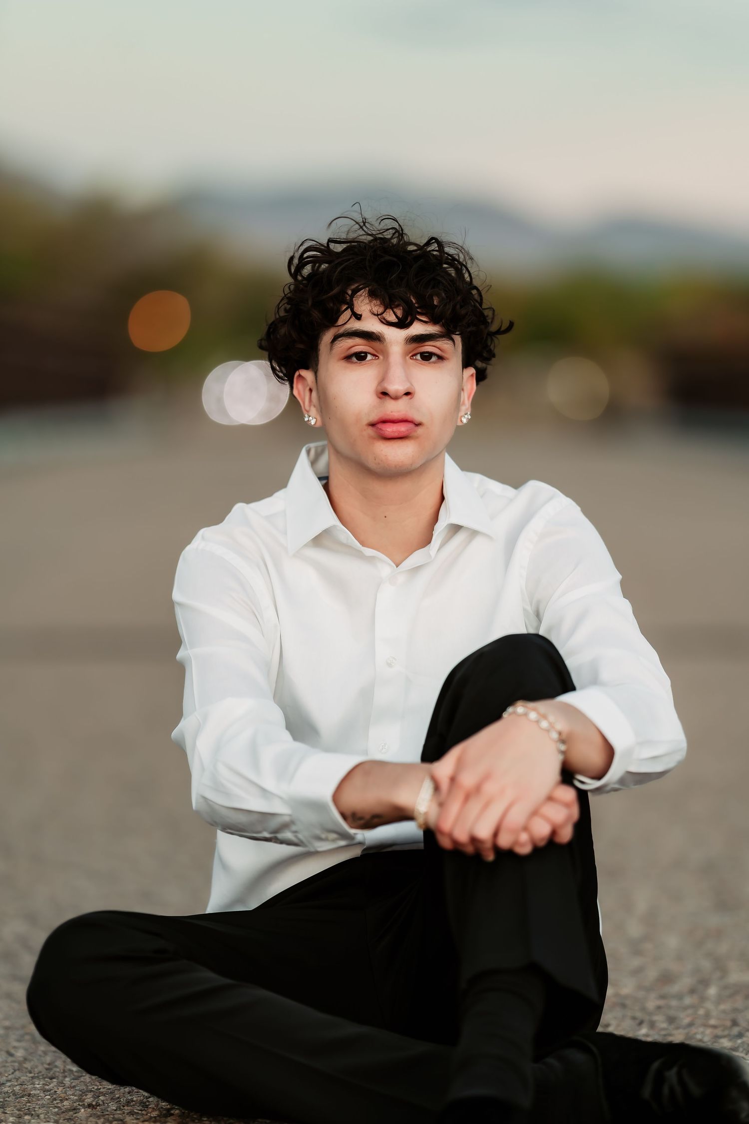 Stylish portrait on pavement wearing white shirt and black pants with mountains in background.
