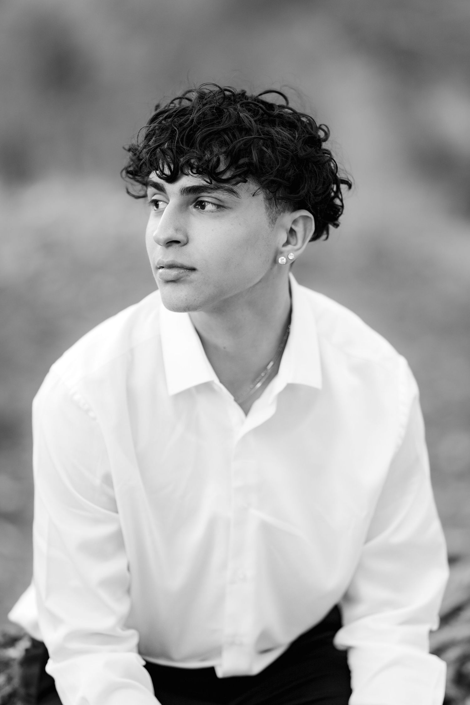 Portrait of someone in a white button-down shirt with curly dark hair against a blurred background.