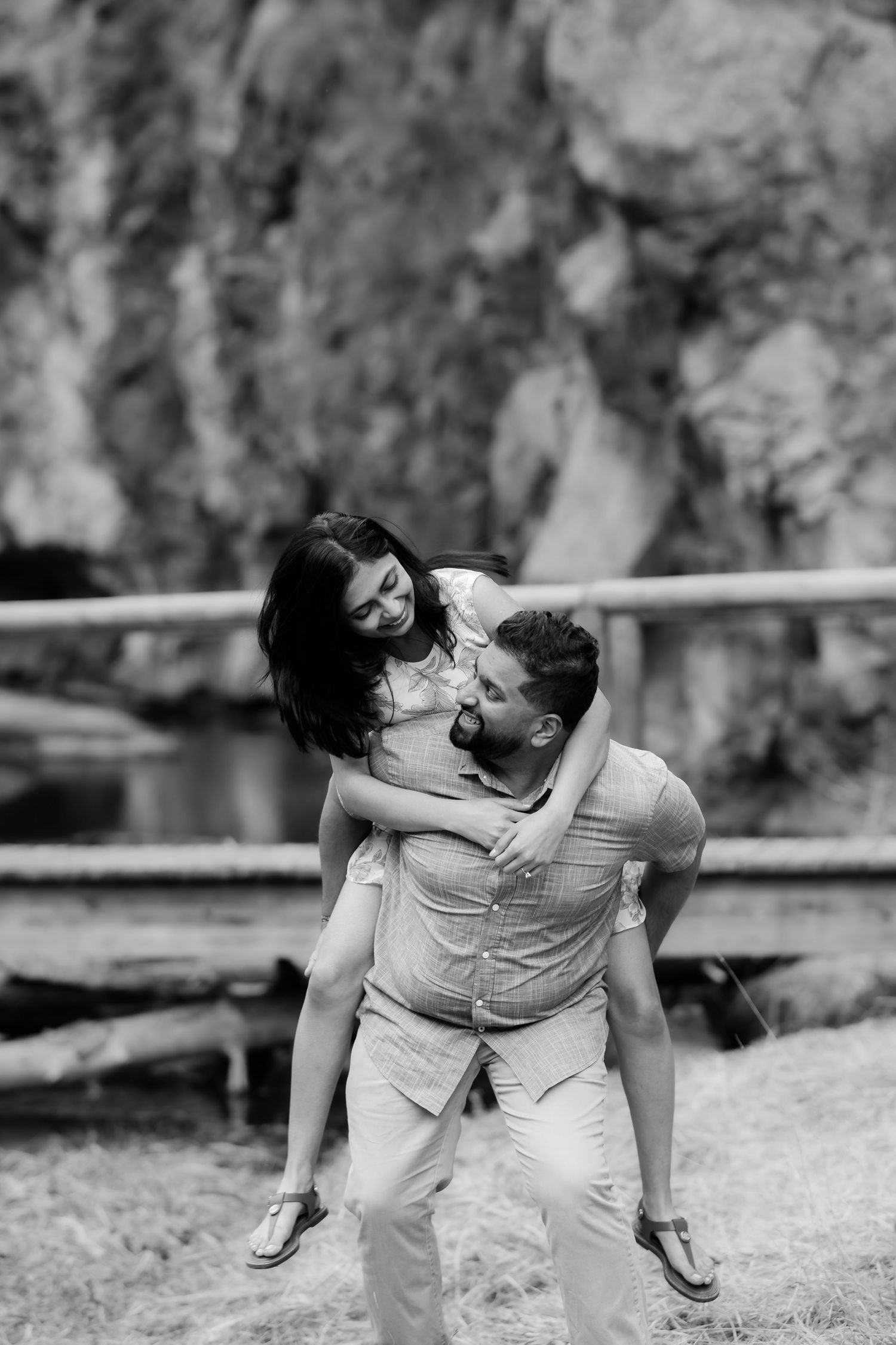 A playful black and white portrait shows a piggyback ride moment against a rocky cliff backdrop.