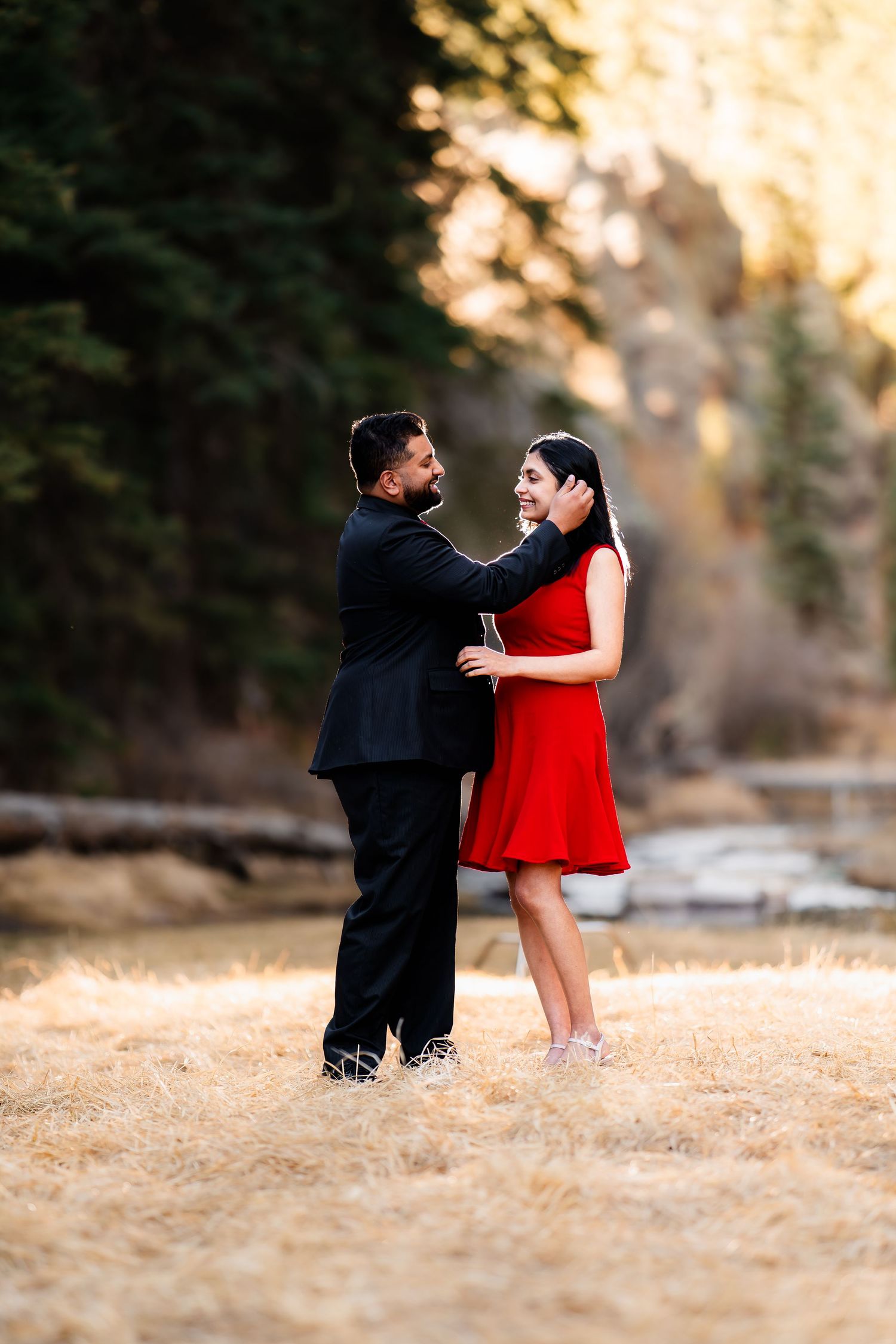 A romantic couple in formal attire dancing together at sunset in a natural outdoor setting.